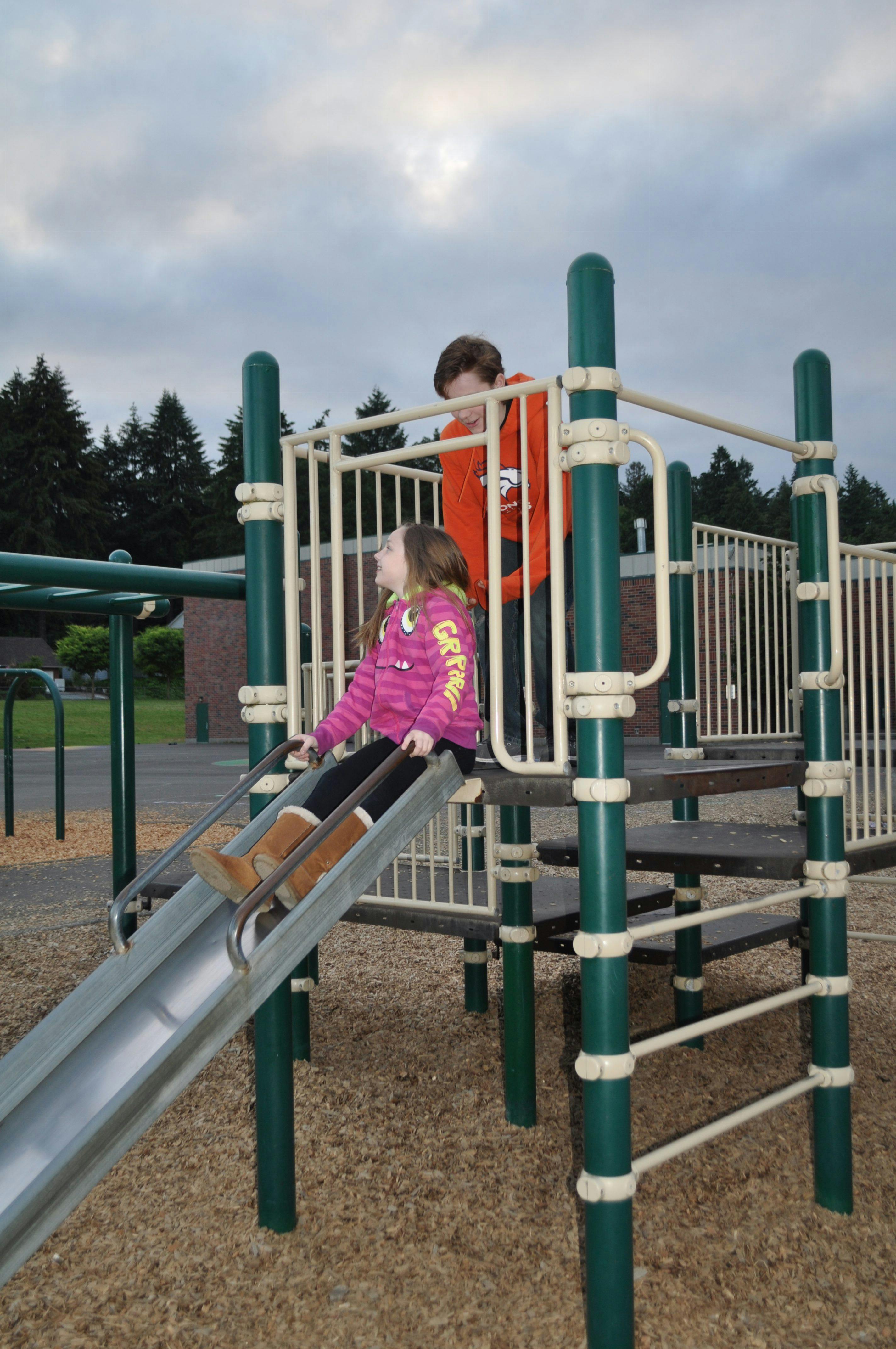 Child on a slide and another child standing on a playground structure