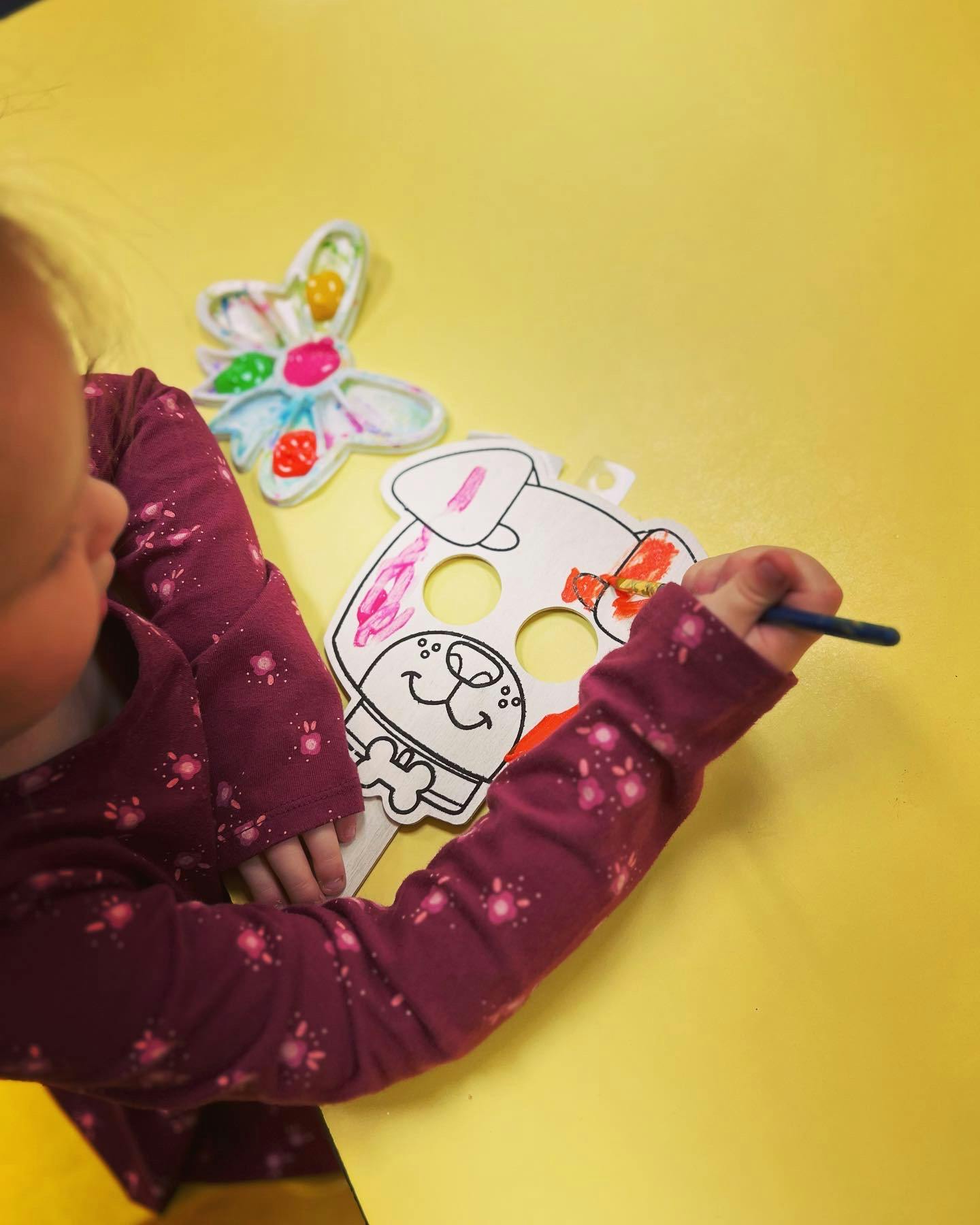 Child painting a dog mask on a yellow table