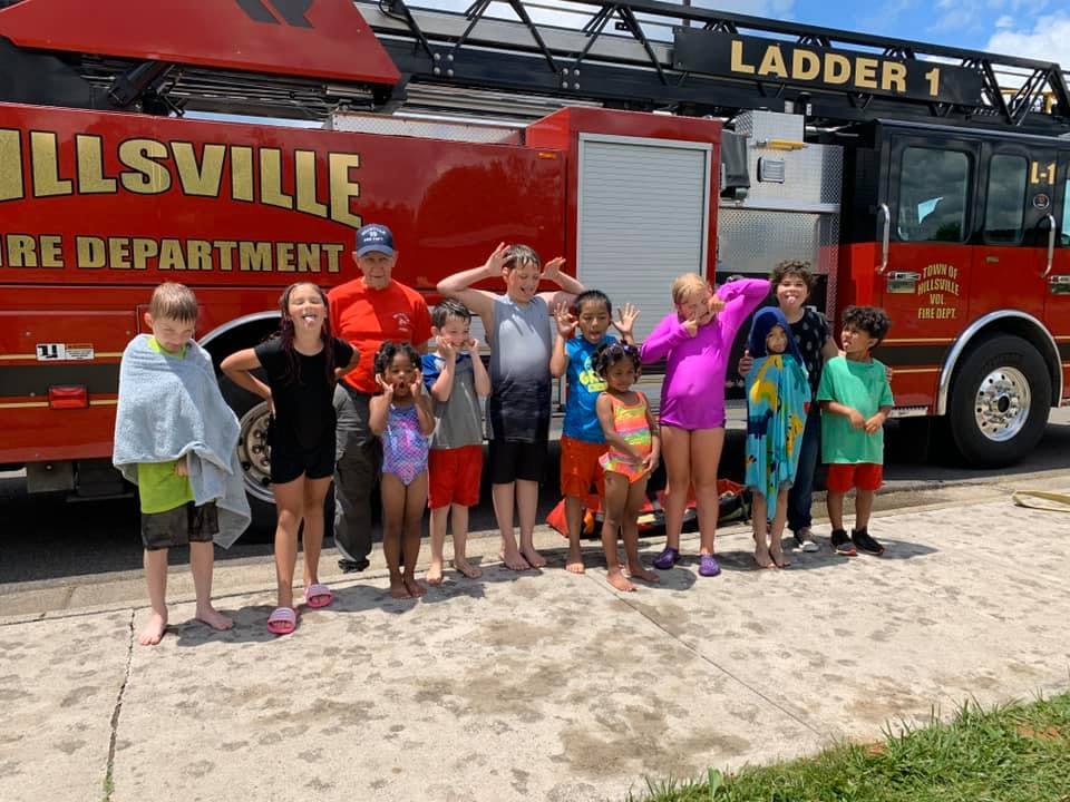 Adult and children in swimsuits posing in front of a fire truck