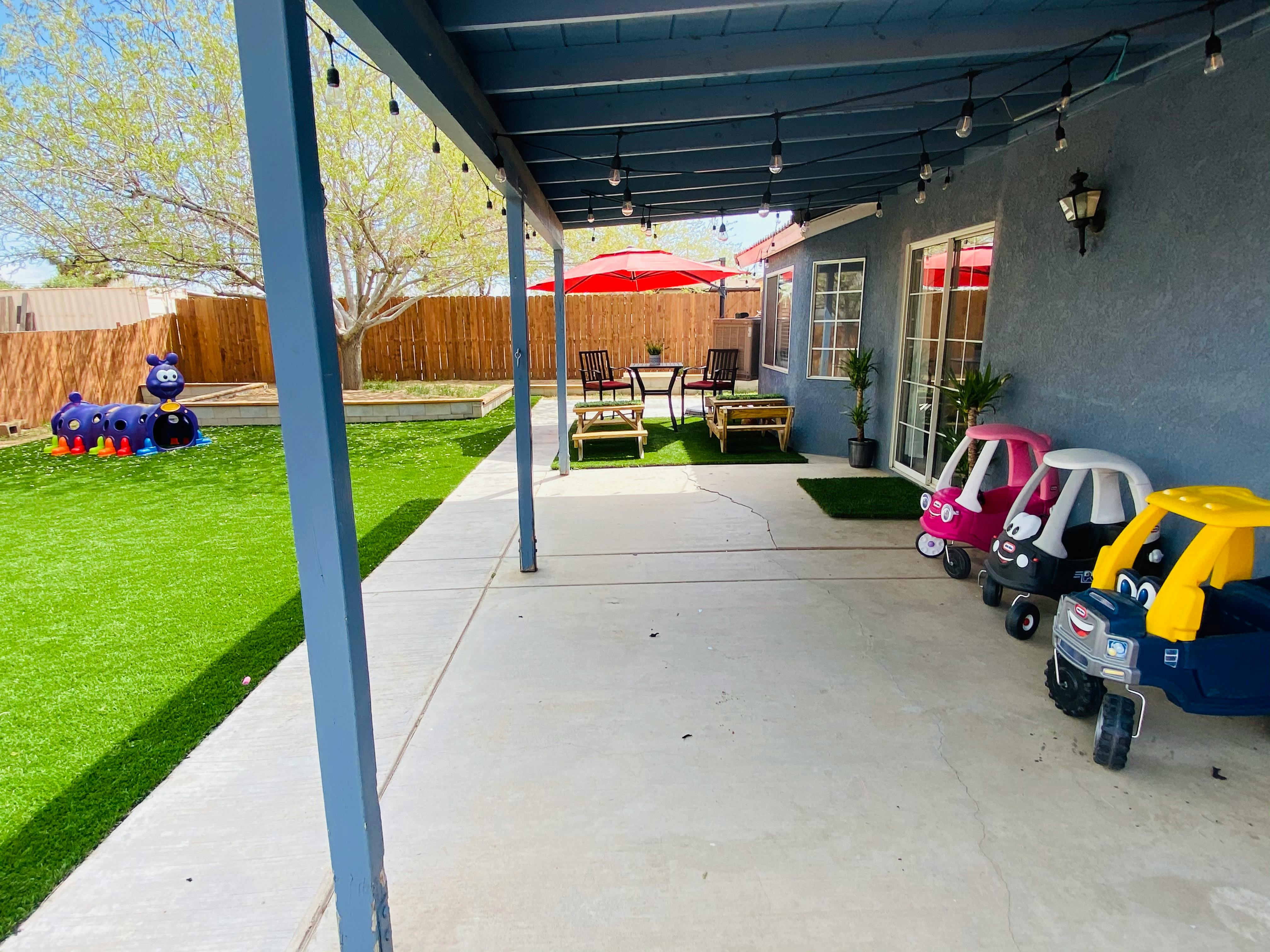 Patio with toy cars and a grassy yard with play equipment