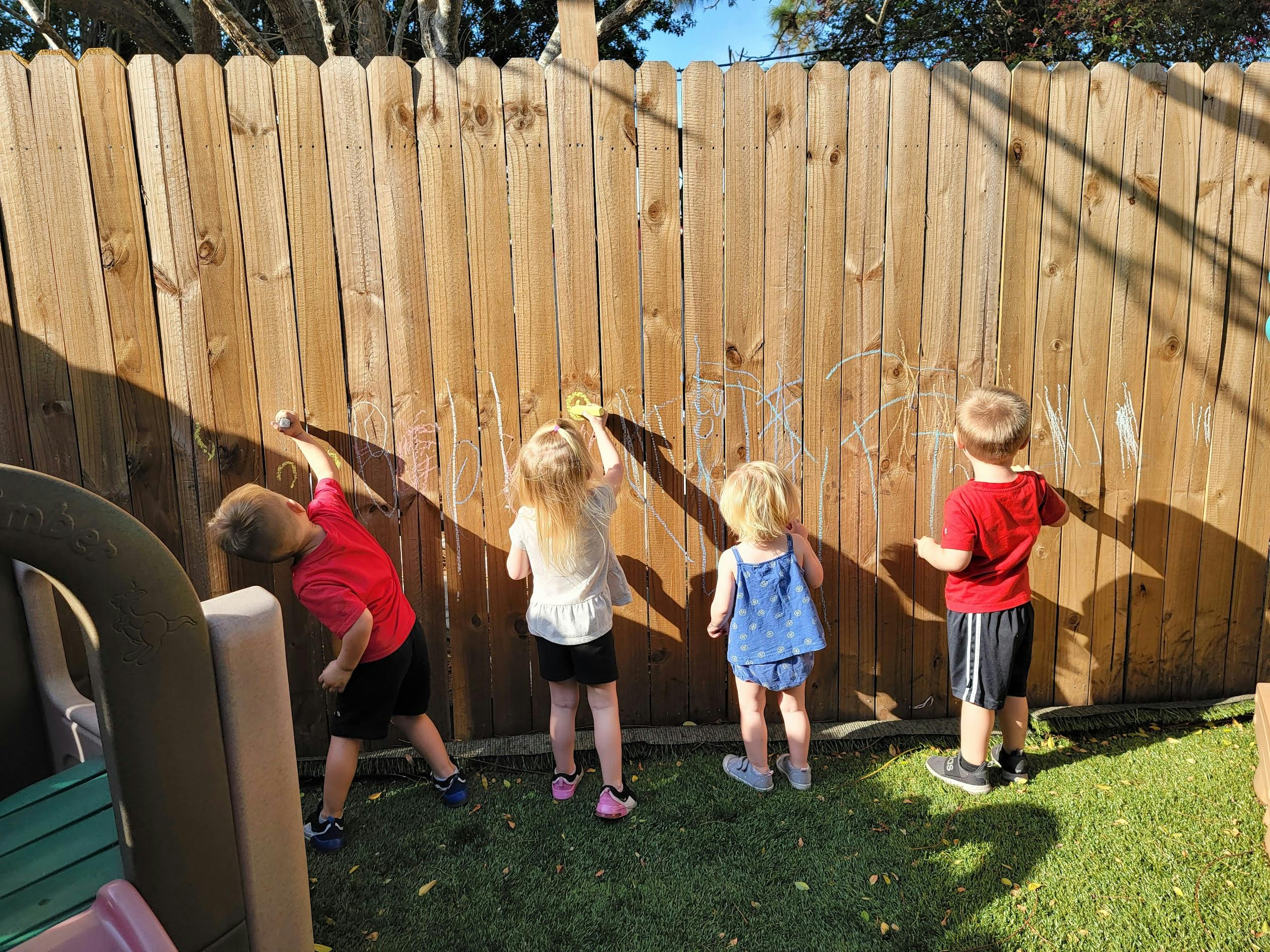 Four children drawing on a wooden fence