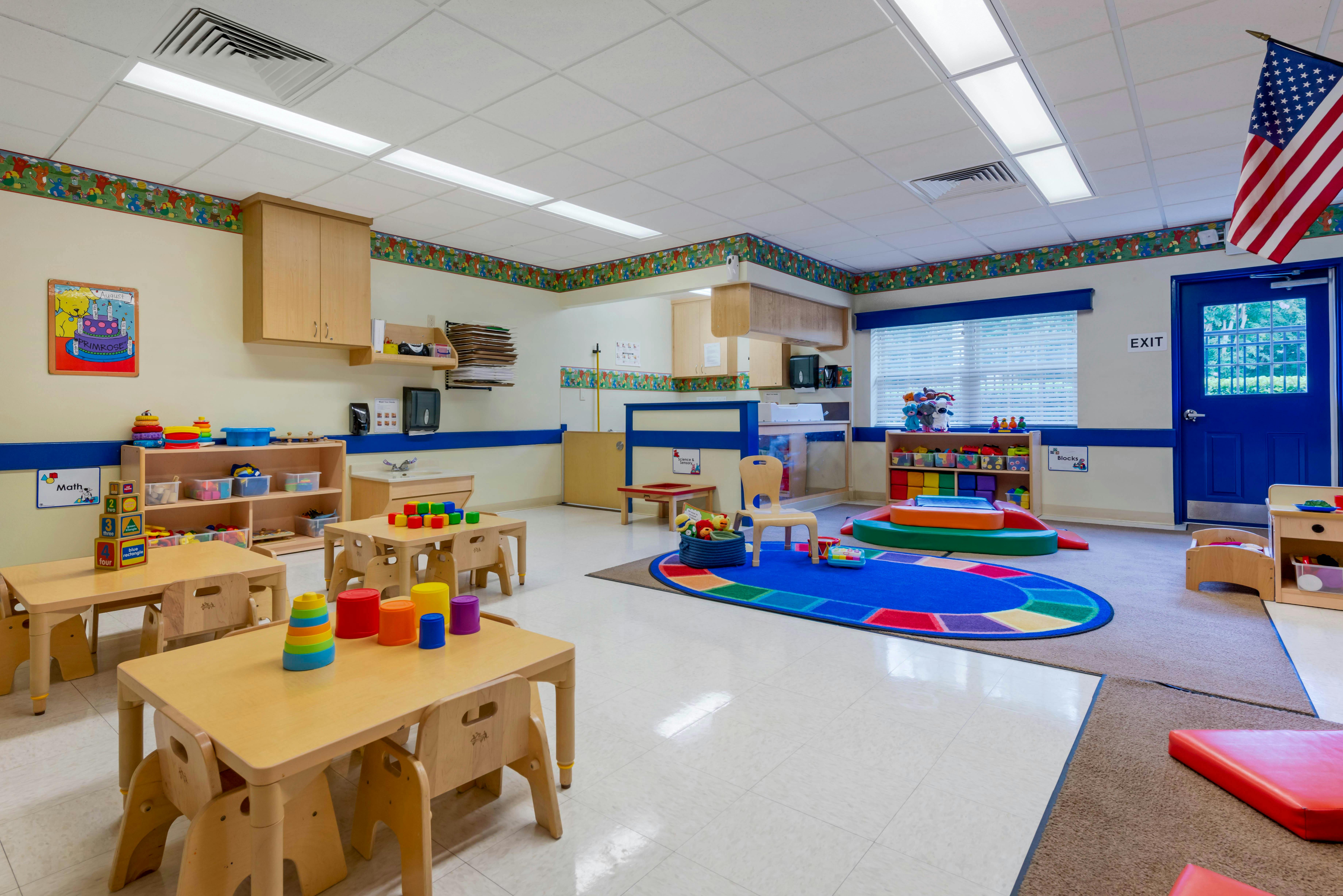 Classroom with small tables and chairs, toys, and blue rug