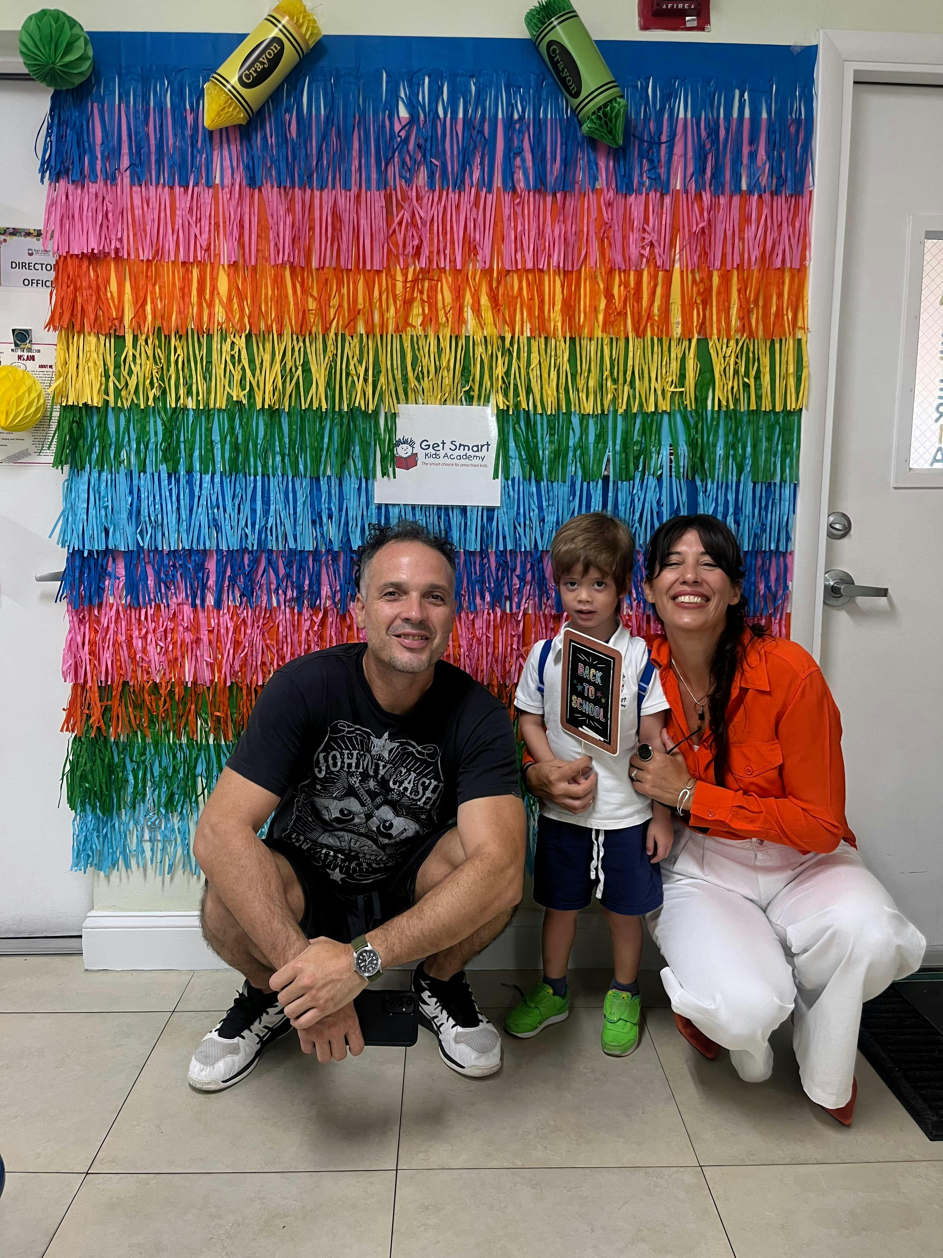 Two adults and a child posing in front of a colorful fringed backdrop