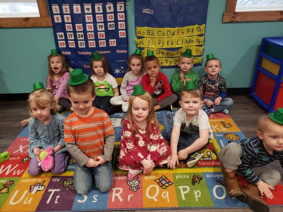 Group of children wearing green hats sitting on a colorful rug