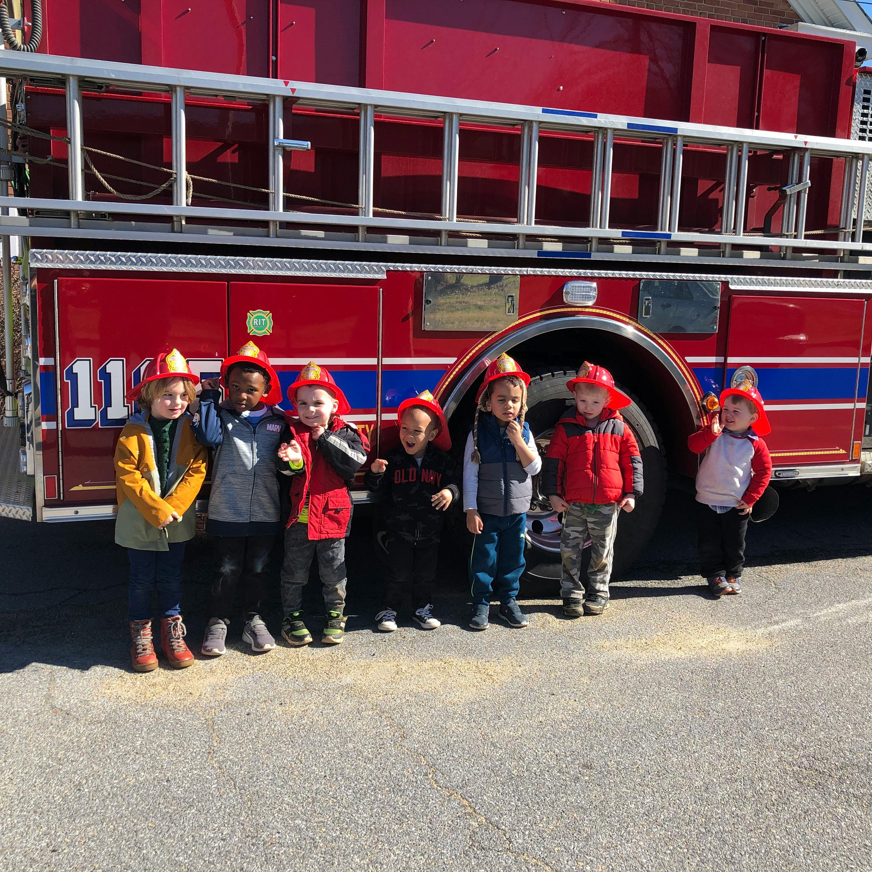 Children wearing fire hats standing in front of a fire truck