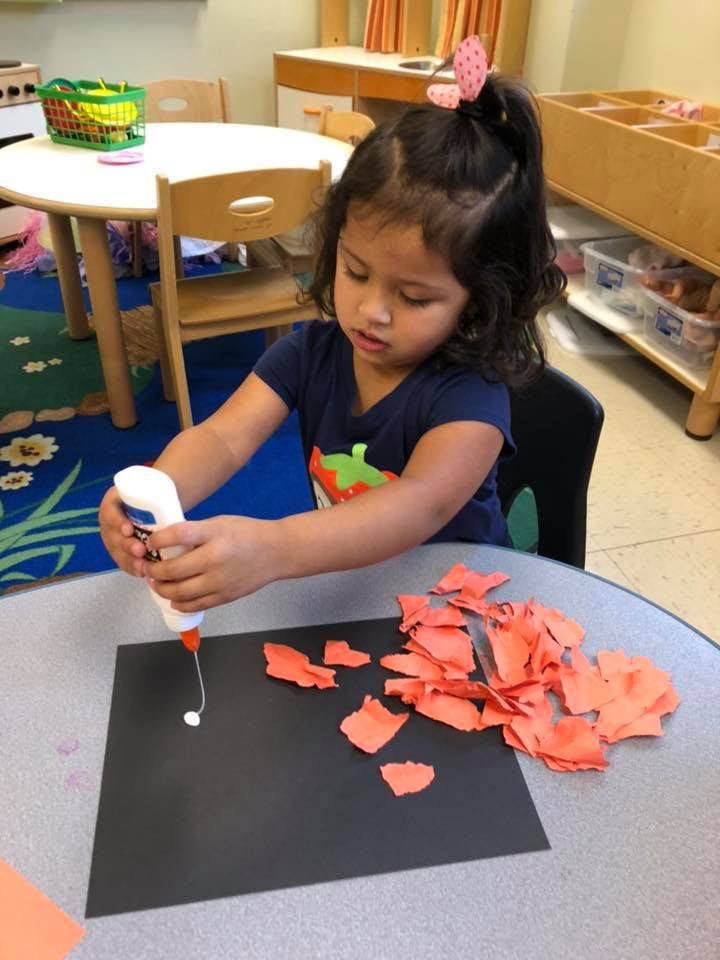 Child applying glue to black paper with orange paper scraps