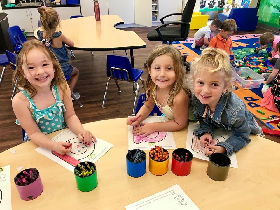 Three children coloring at a table in a classroom