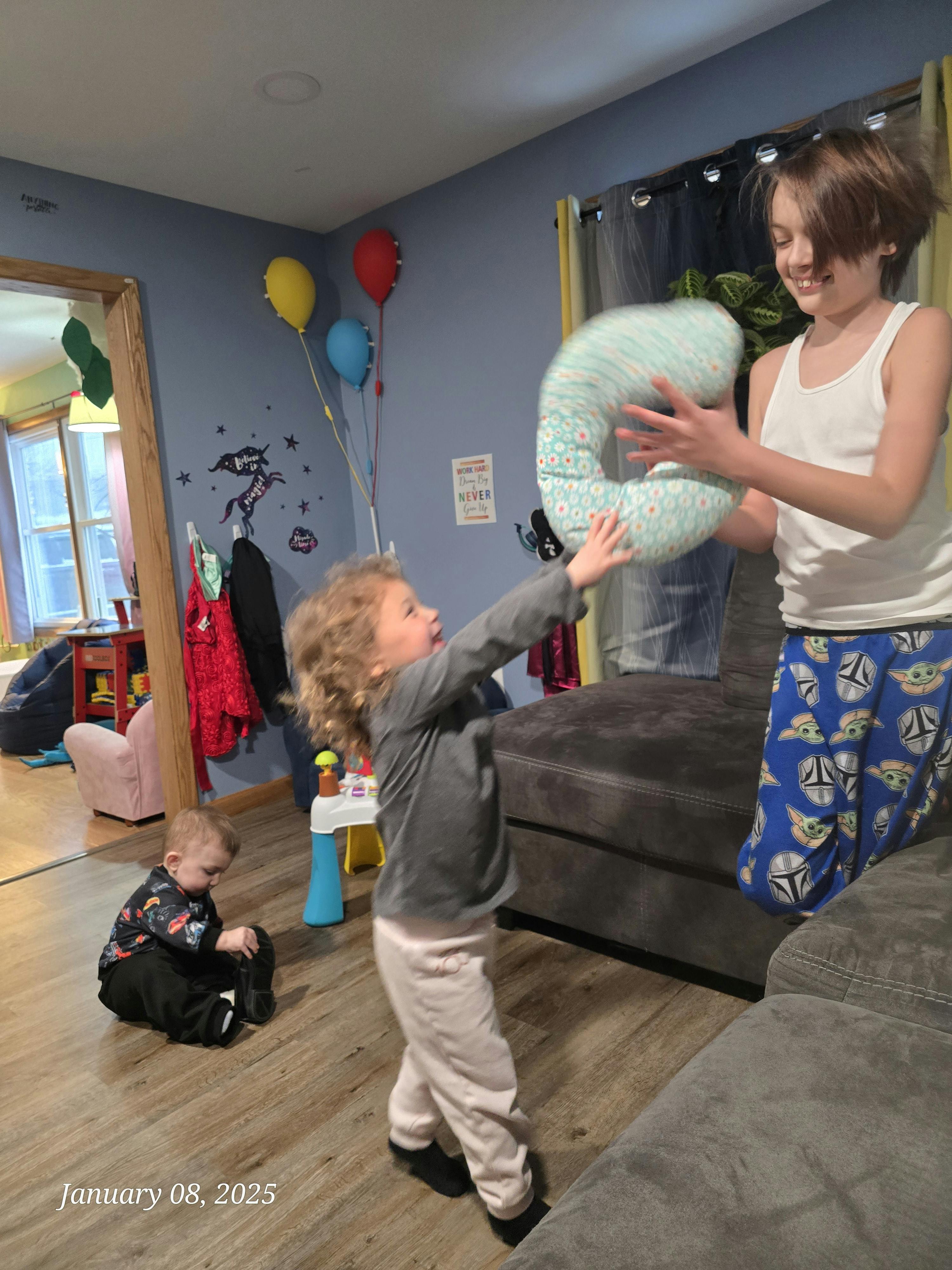 Two children playing with a large pillow, another child on the floor