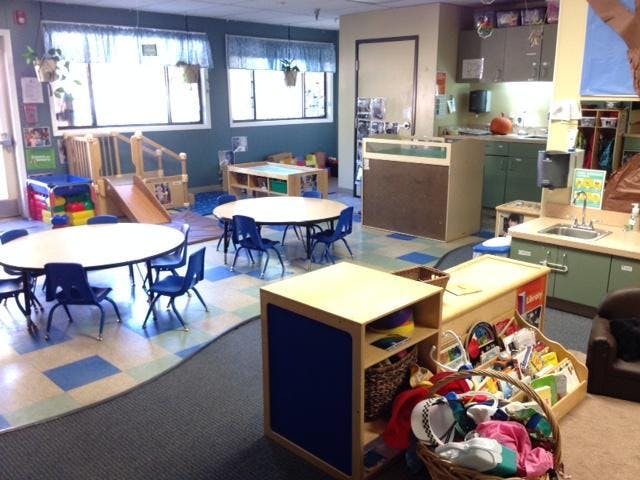 empty classroom with small tables and chairs, play structures, and a sink area