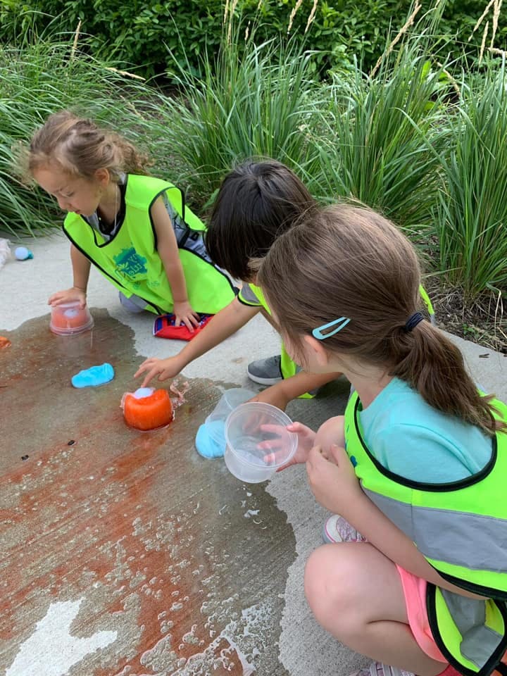 Three children playing with water and containers on a wet surface outdoors