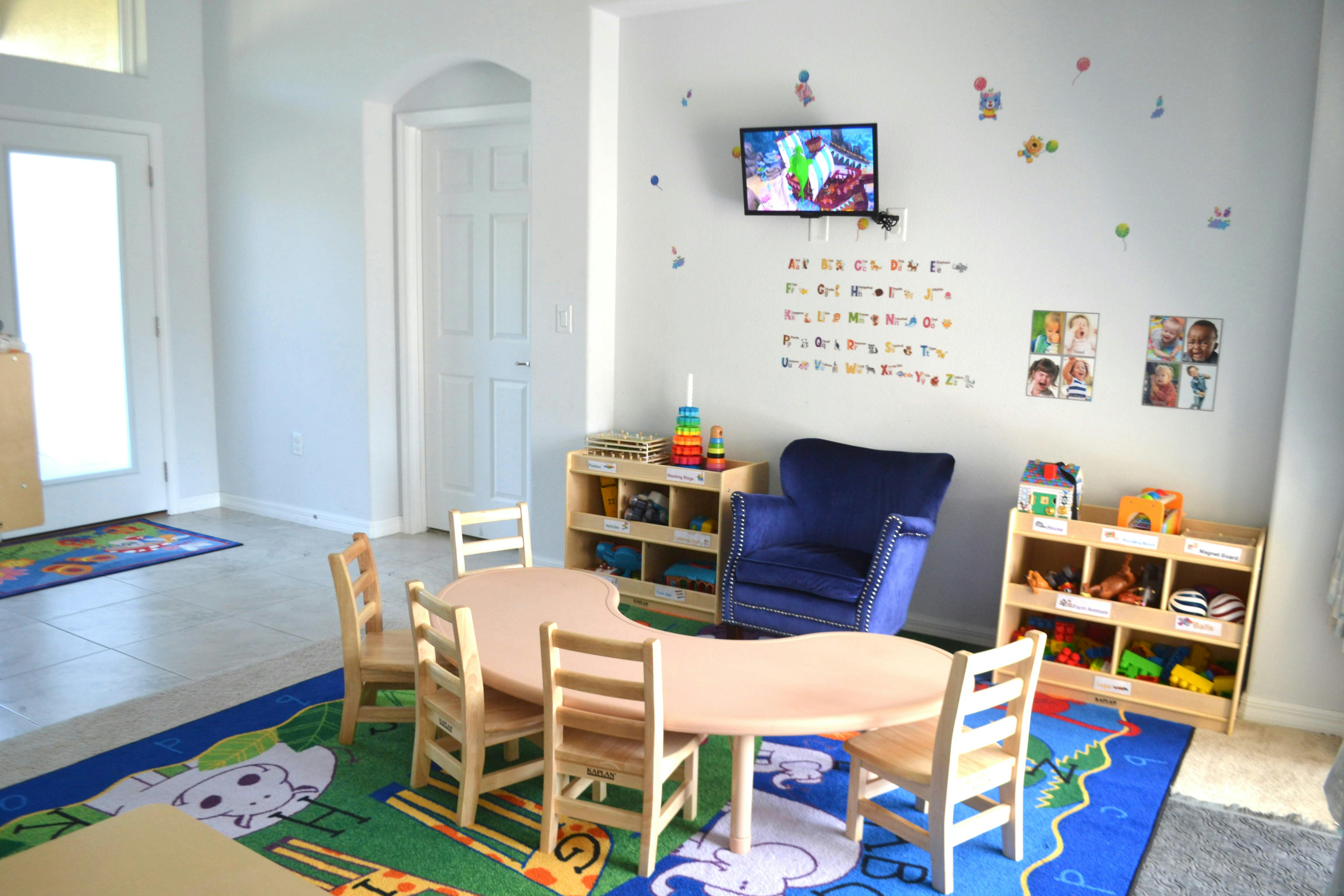 Children's play area with small tables and chairs, shelves with toys, and a TV