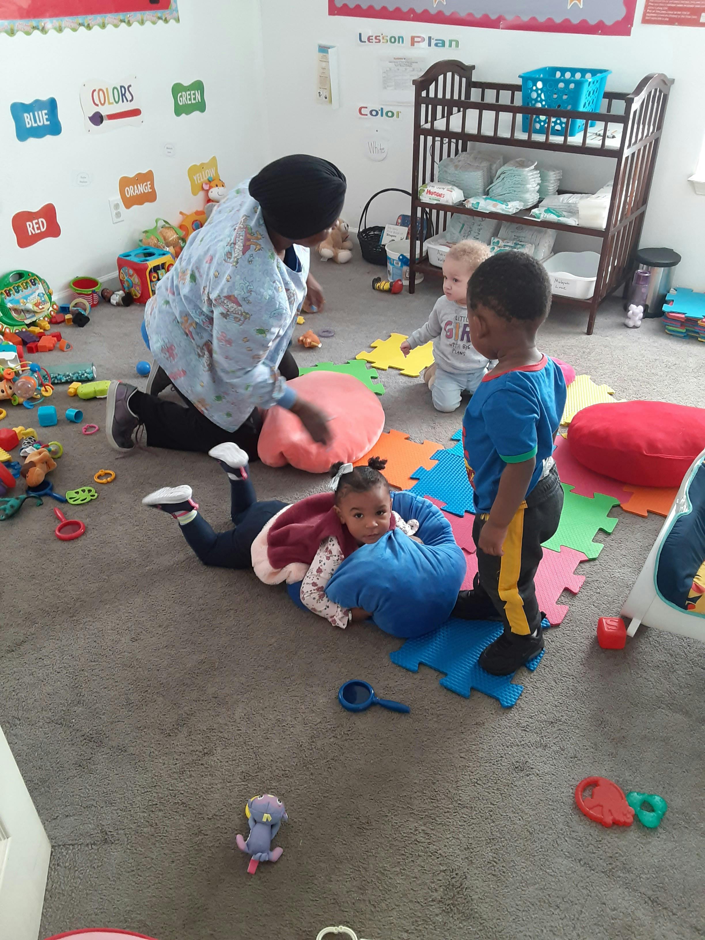 Adult kneeling with three children playing on the floor in a room