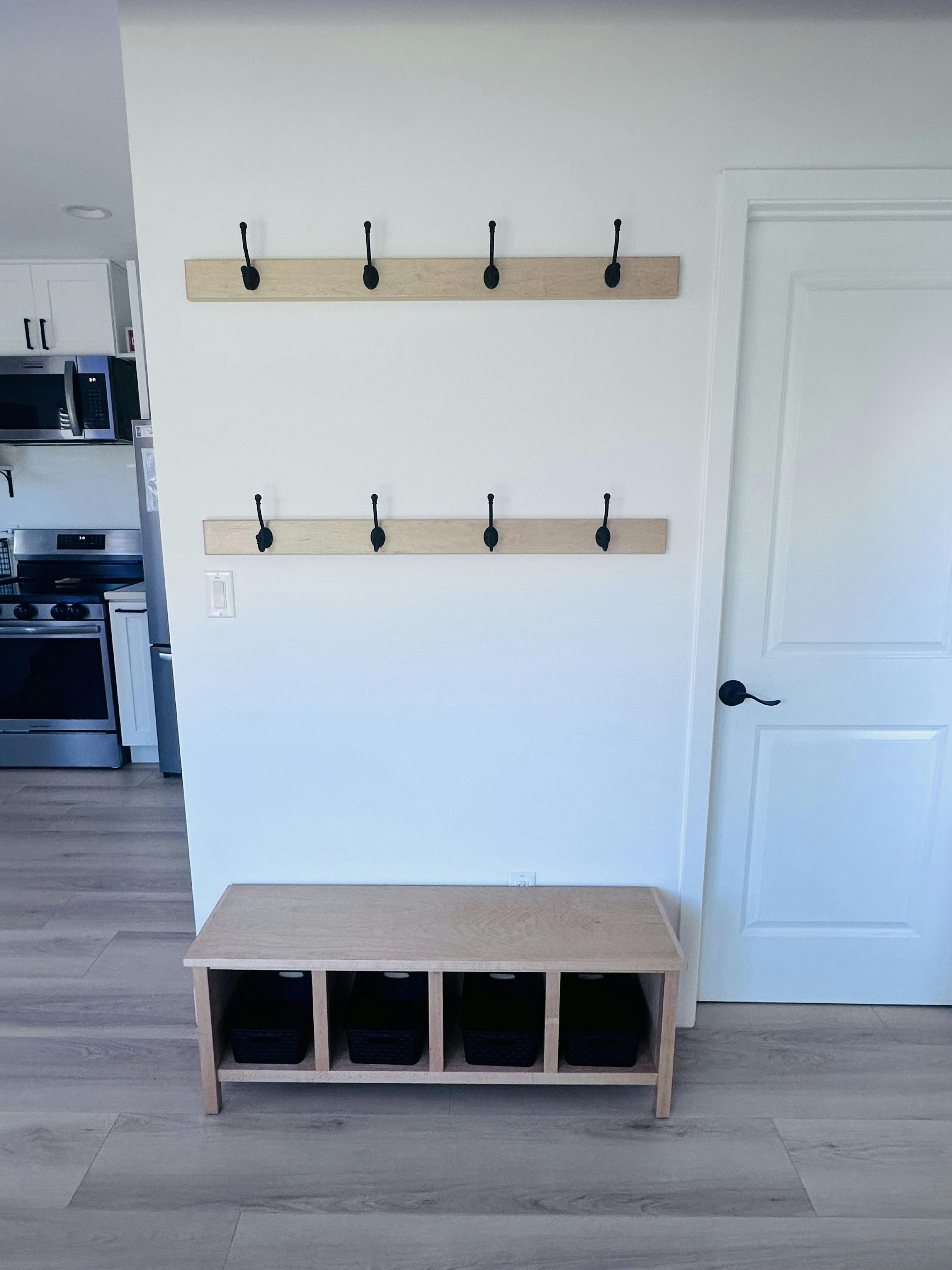 Wooden entryway bench with storage bins under wall-mounted coat hooks