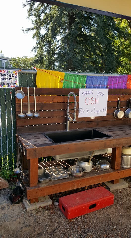 Outdoor wooden play kitchen with sink, faucet, and various utensils