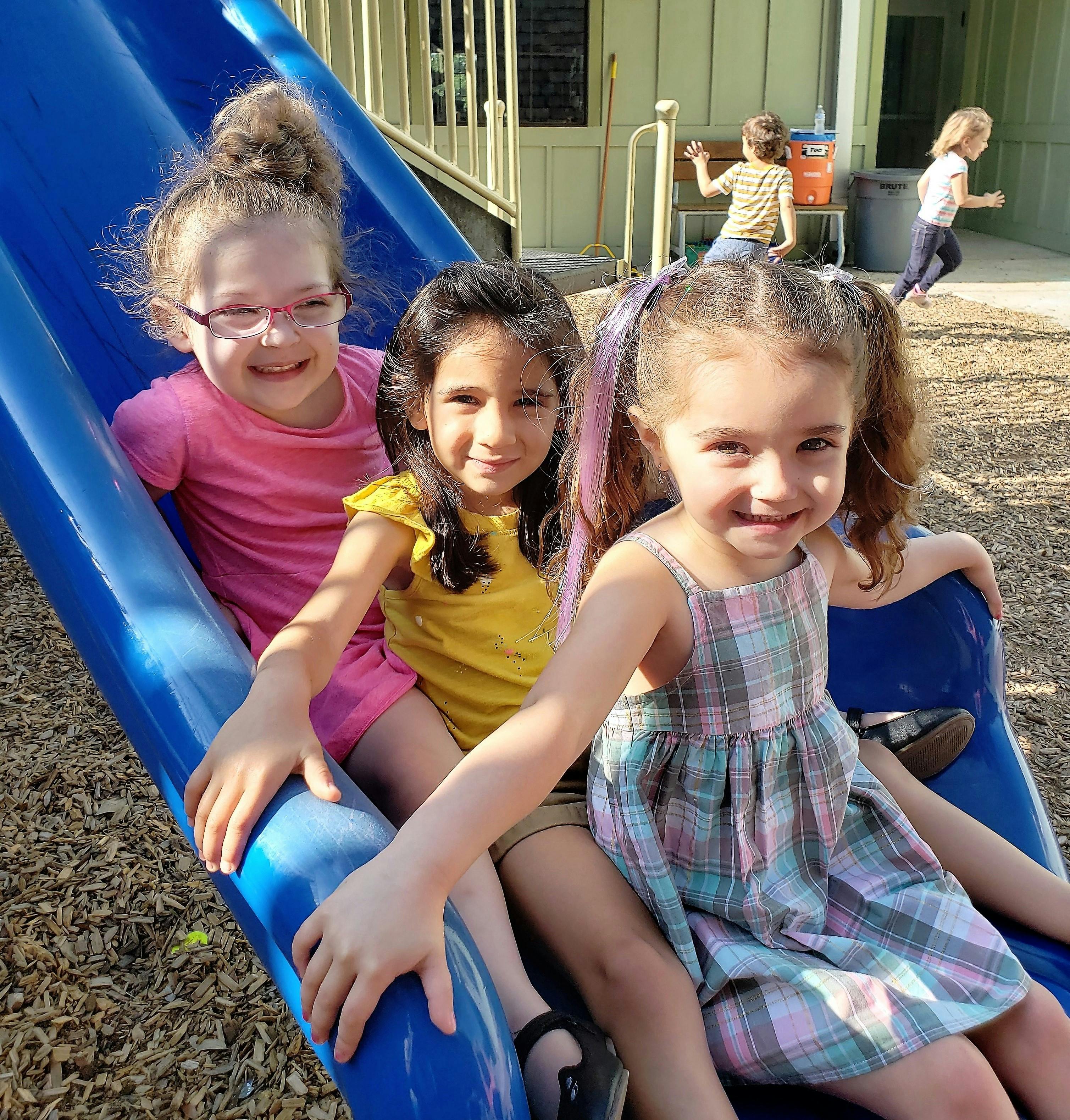 Three children sitting on a blue slide