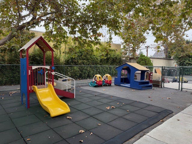 Playground with a red and yellow slide, a blue playhouse, and ride-on toys