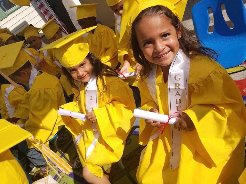 Children in yellow graduation gowns and caps holding diplomas