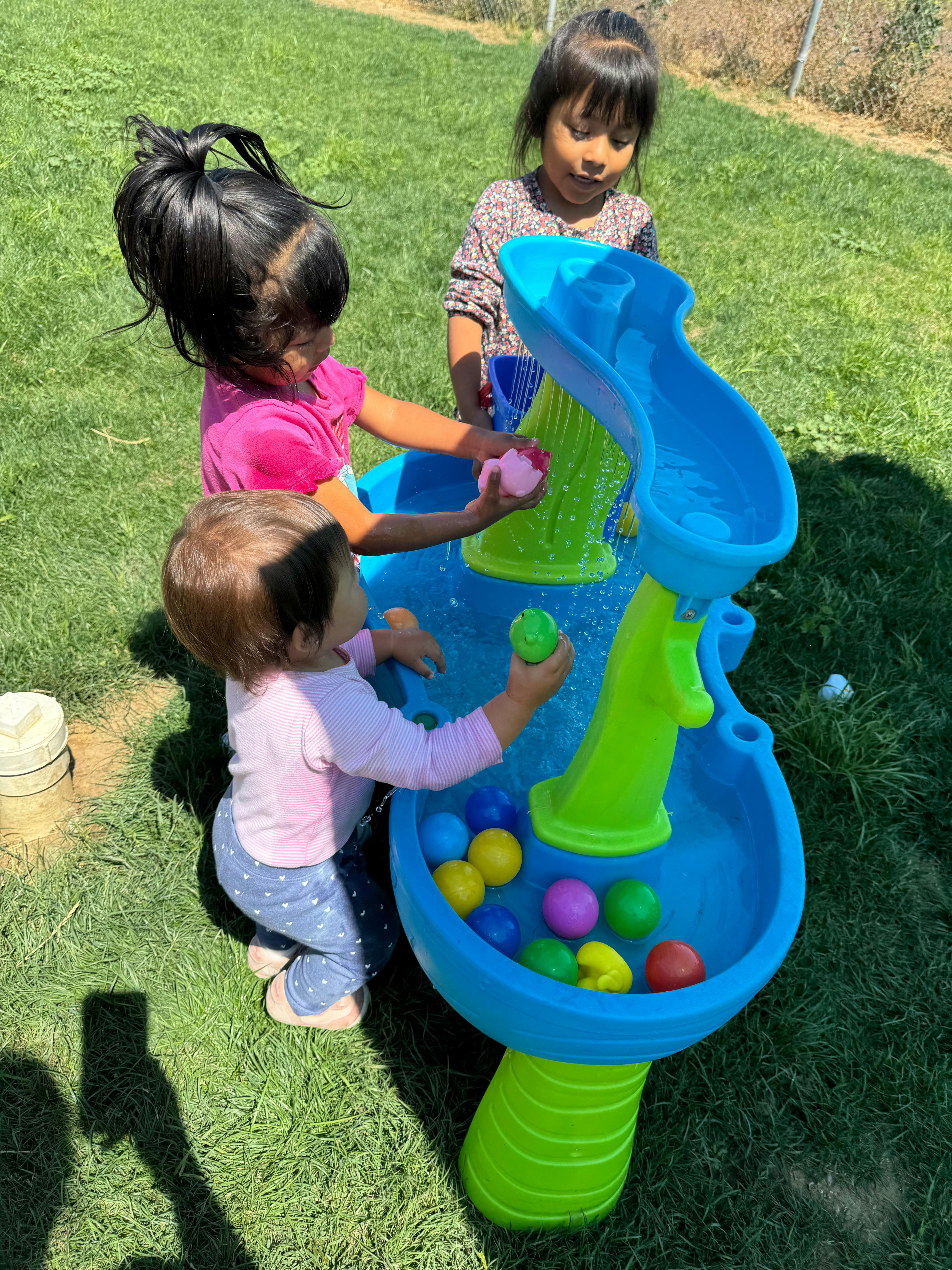 Three children playing with a water table and colorful balls outdoors