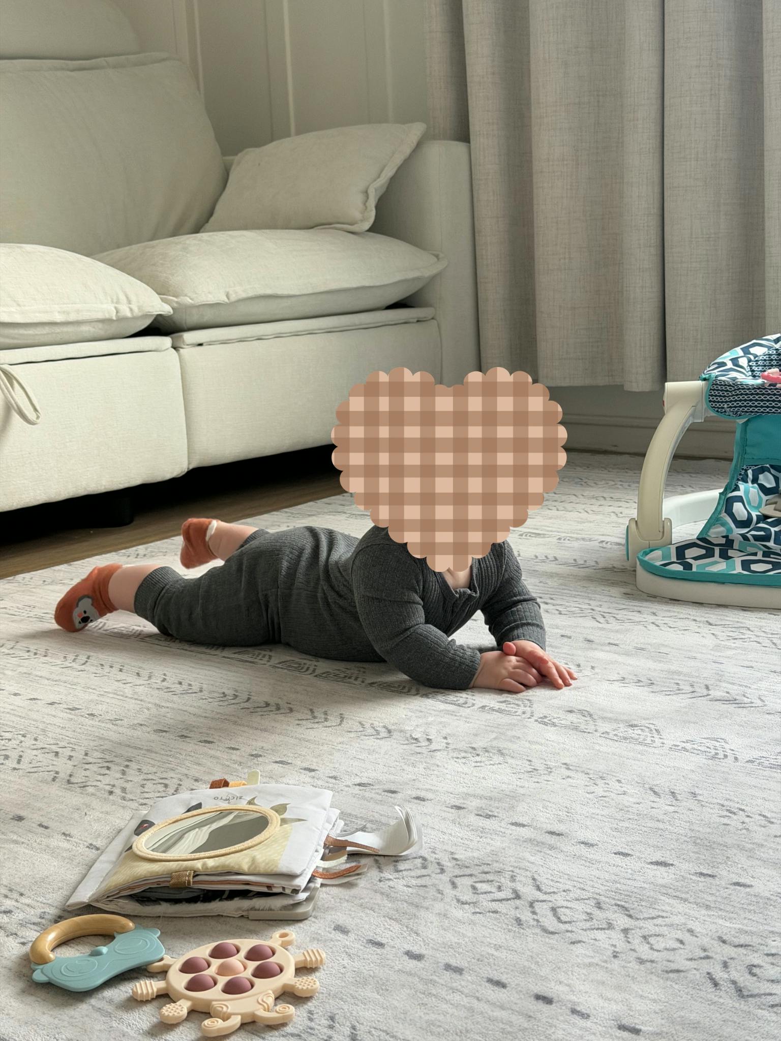 Child on hands and knees on a rug next to toys and a couch