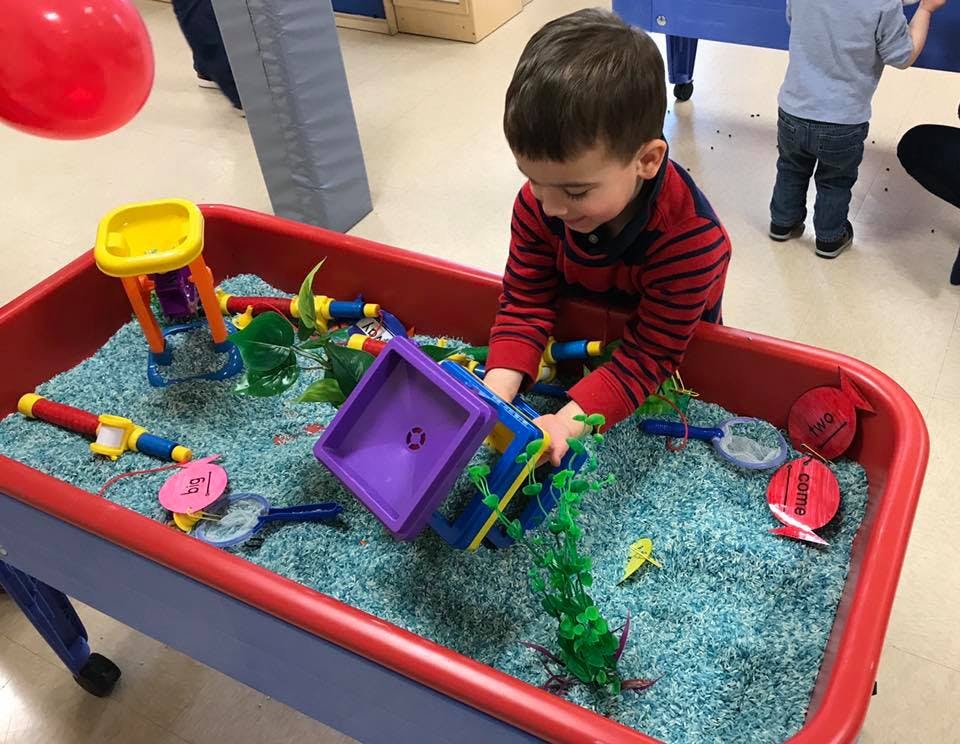 Child playing with toys in a sensory bin filled with blue material