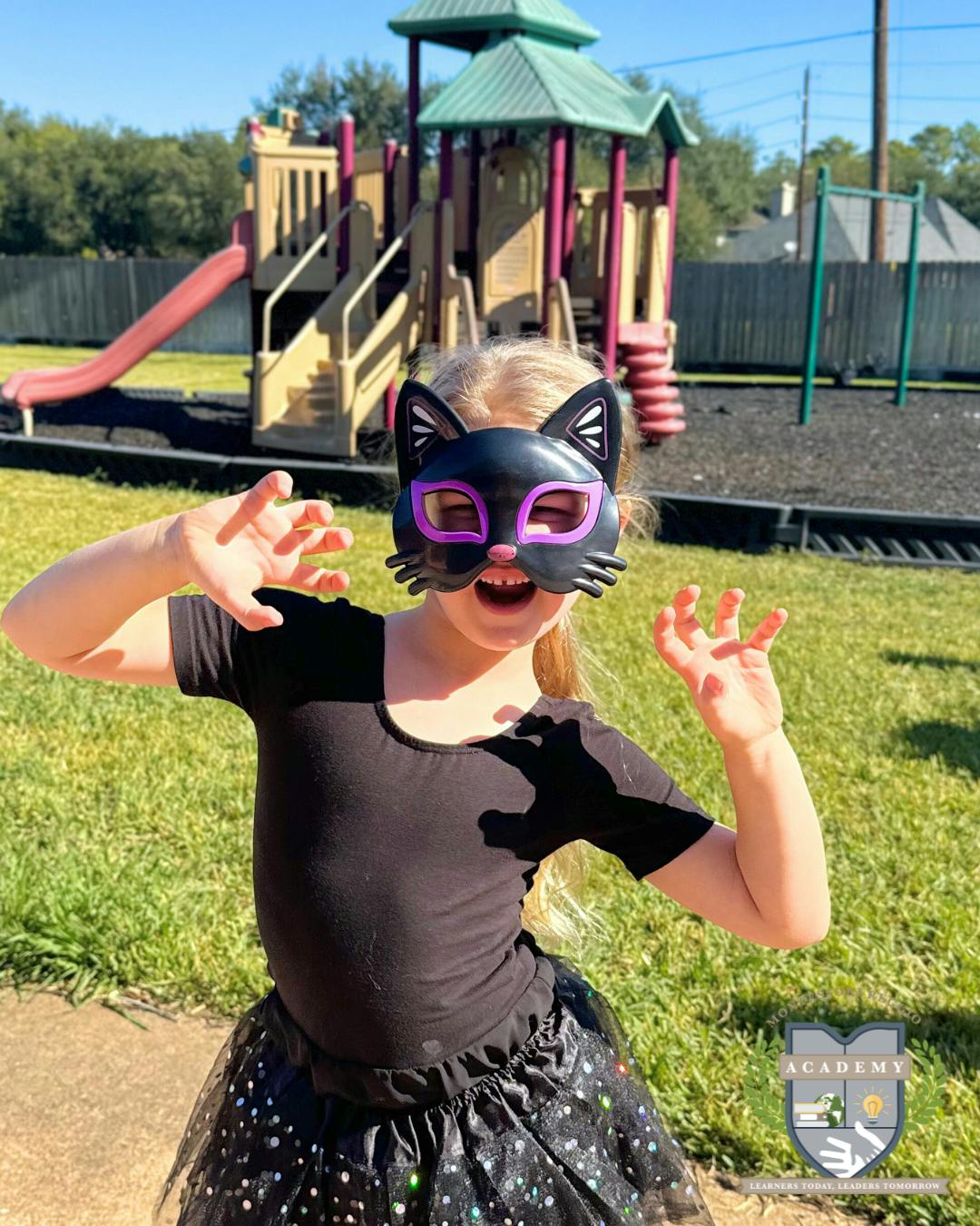 Child in a cat mask with hands raised at a playground