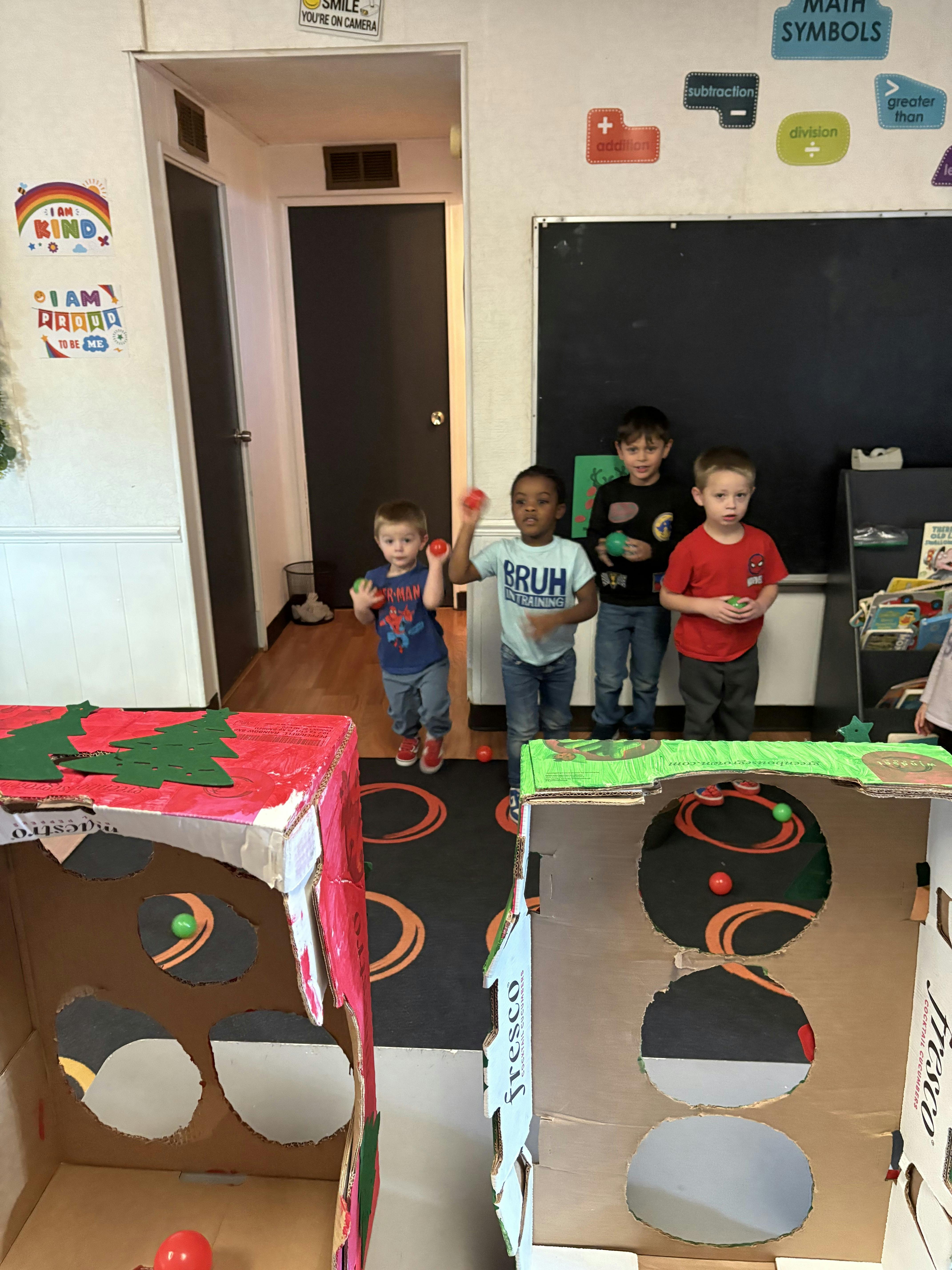 Four children playing with balls and cardboard boxes in a classroom