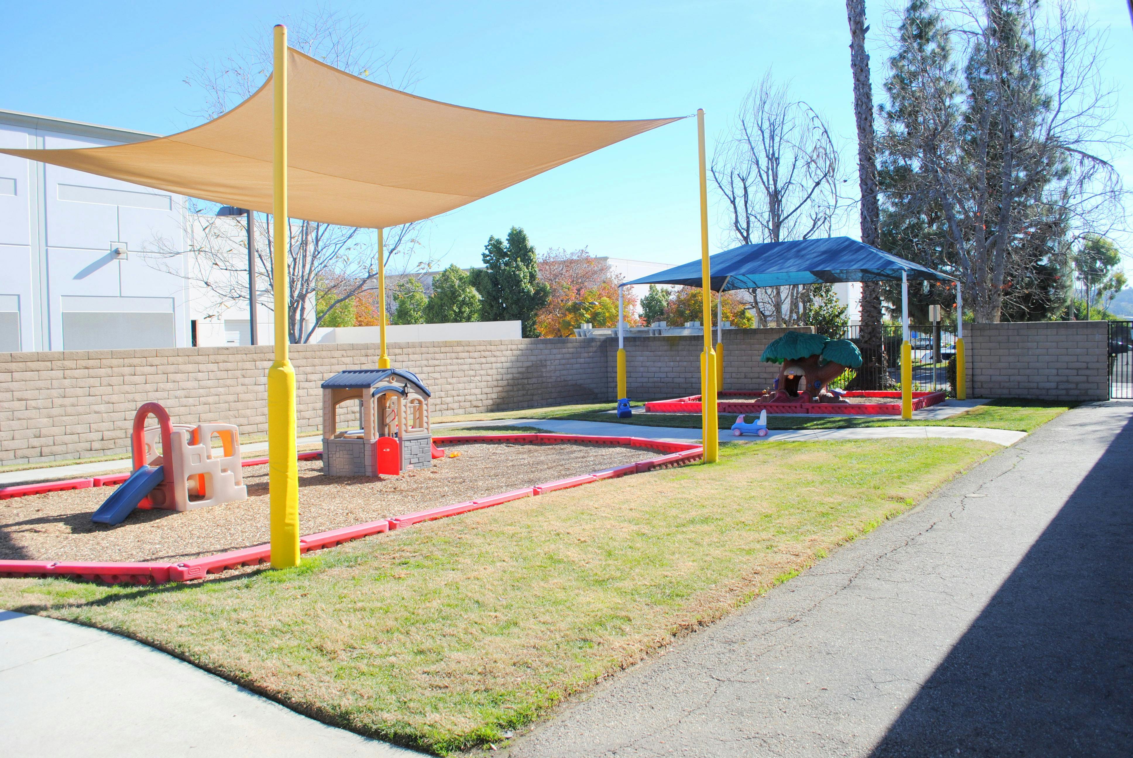 Outdoor playground with sand, play structures, and shade canopies
