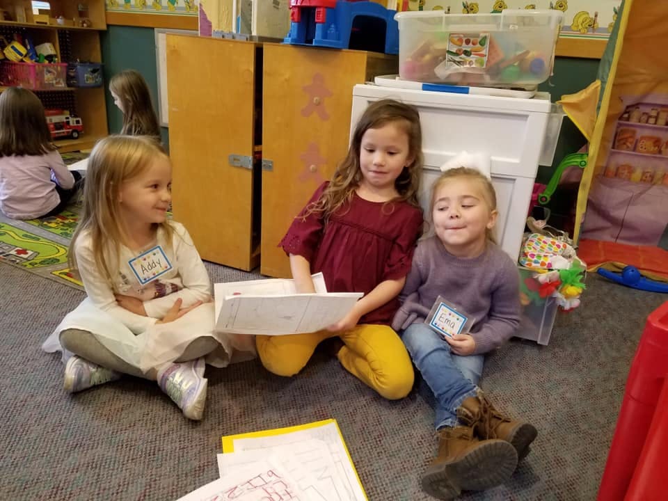 Three children sitting on the floor, one holding a laptop