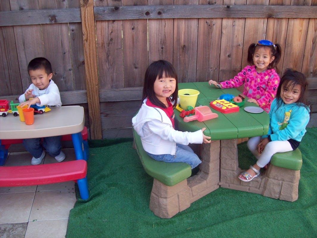 Four children playing with toys at small tables outdoors