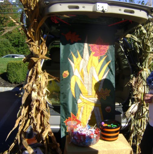 Car trunk decorated with corn stalks and a banner, with candy bowls
