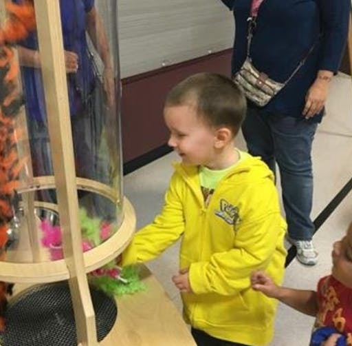 Child in yellow jacket playing with a clear tube