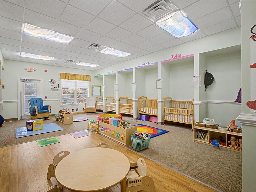 A colorful empty daycare room with cribs, play areas, and small tables