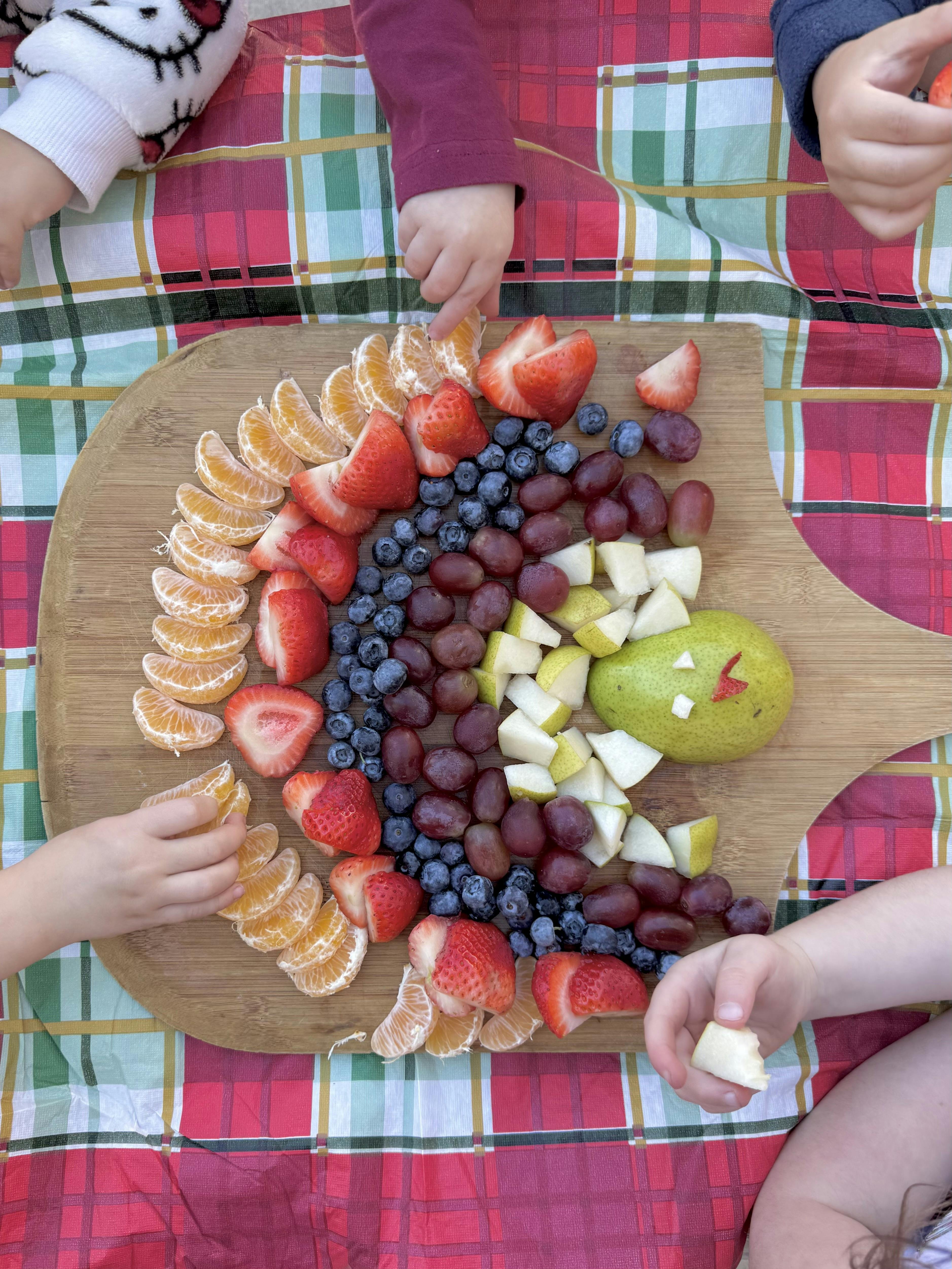 People's hands reaching for fruit arranged on a wooden board