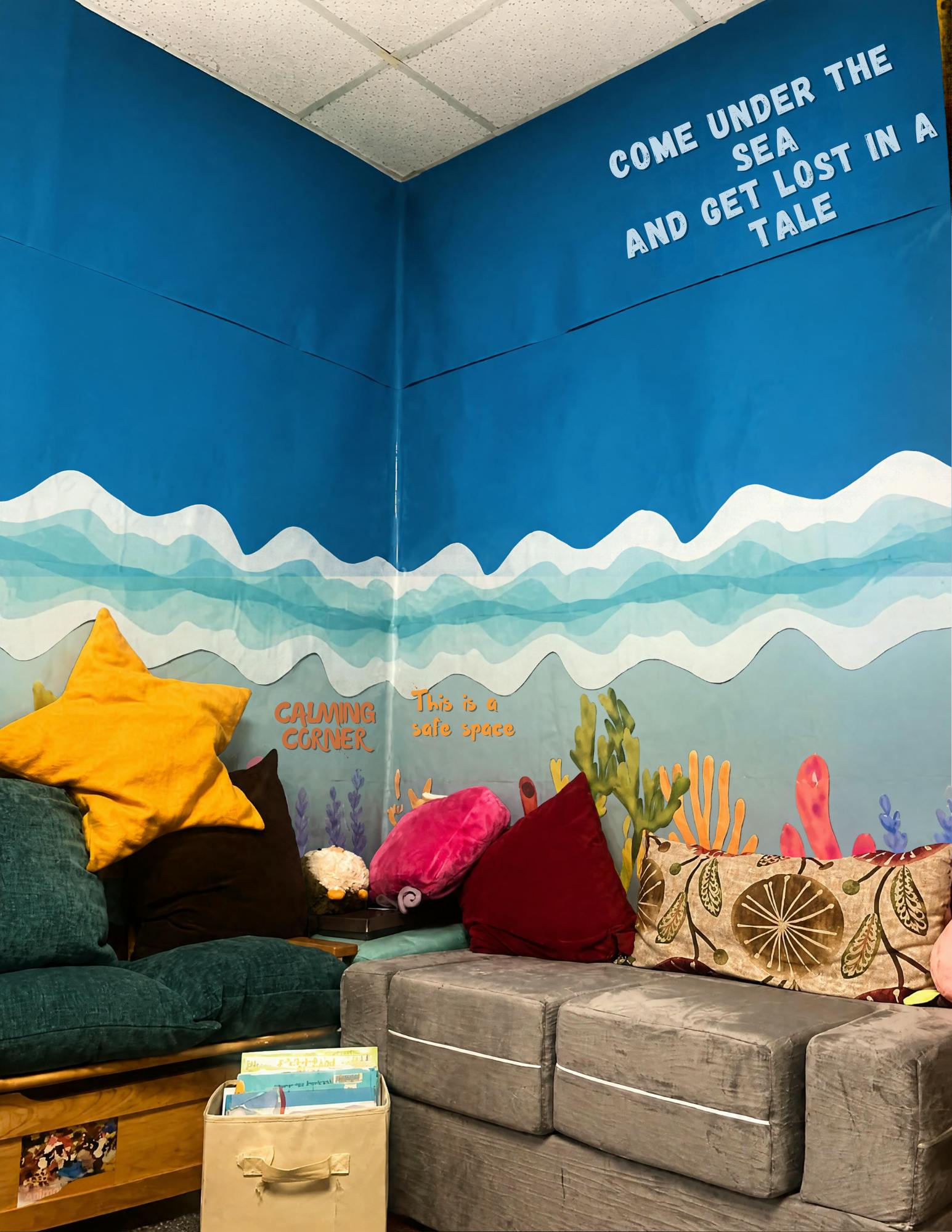 Calming corner with cushions and books under an ocean themed wall decoration