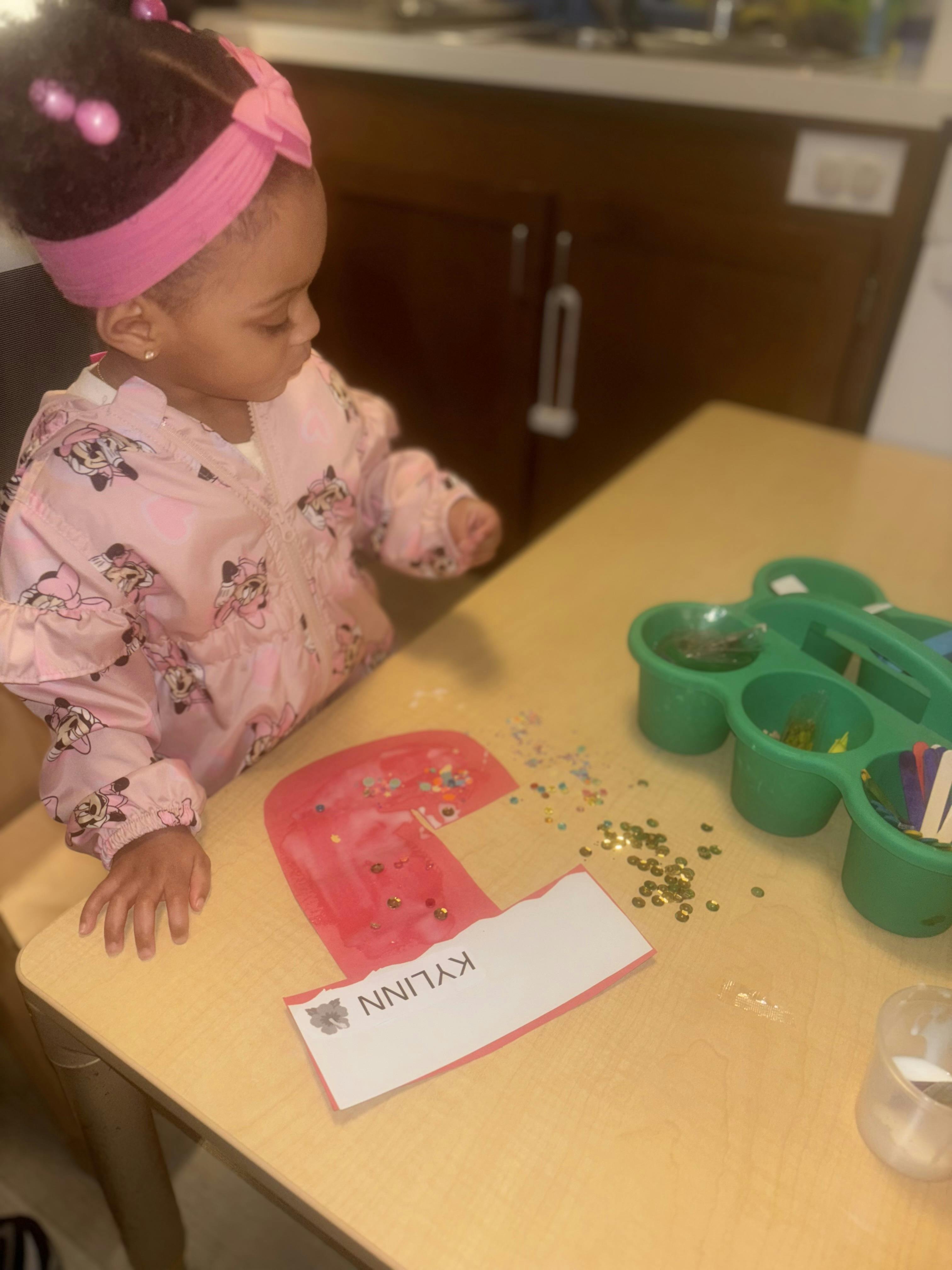 Child at a table with craft supplies and a paper with "KYLINN" written on it