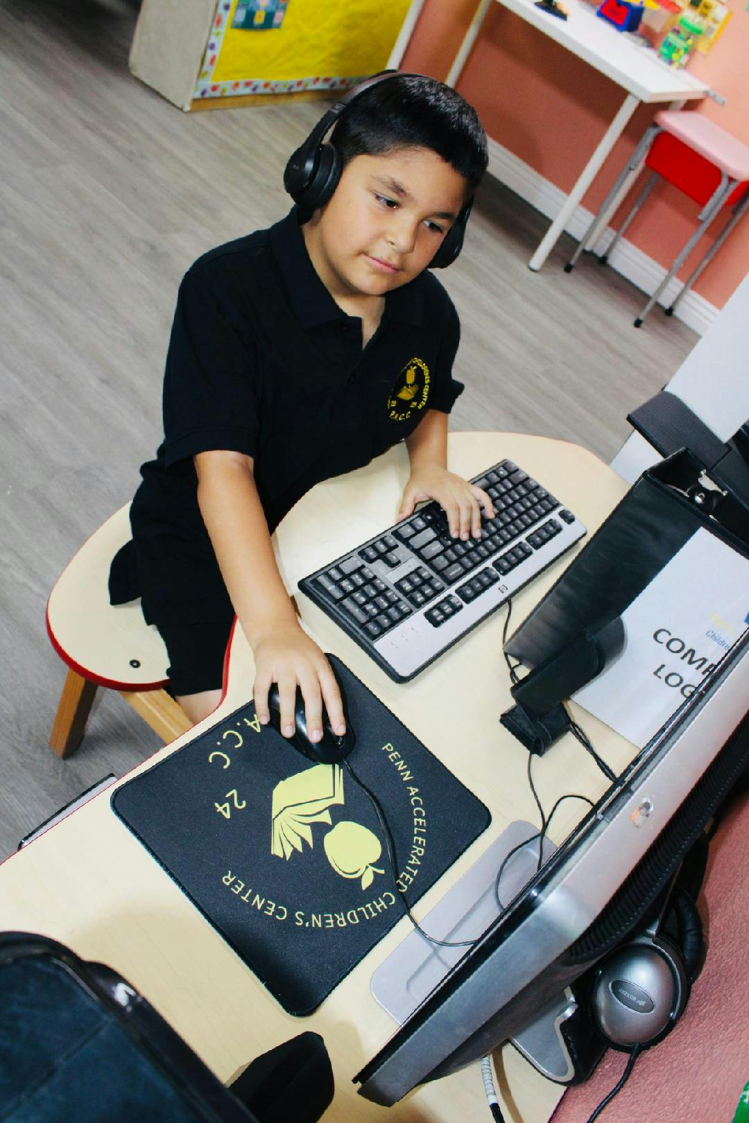 Child wearing headphones using a computer with a keyboard and mouse