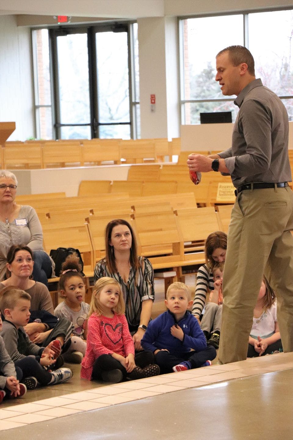 Person speaking to a group of adults and children sitting on the floor