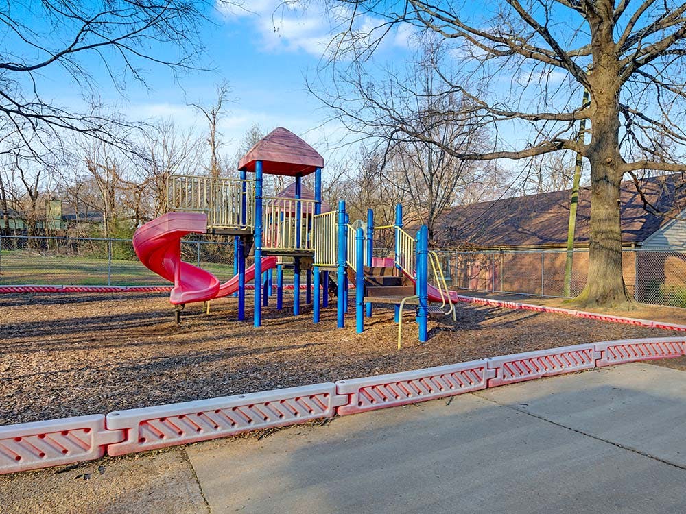 A red and blue playground structure with a slide on wood chips