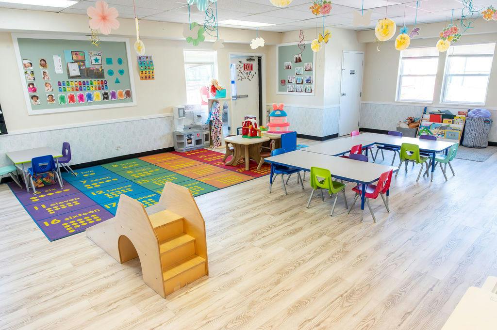 Empty preschool classroom with small tables and chairs and a play slide