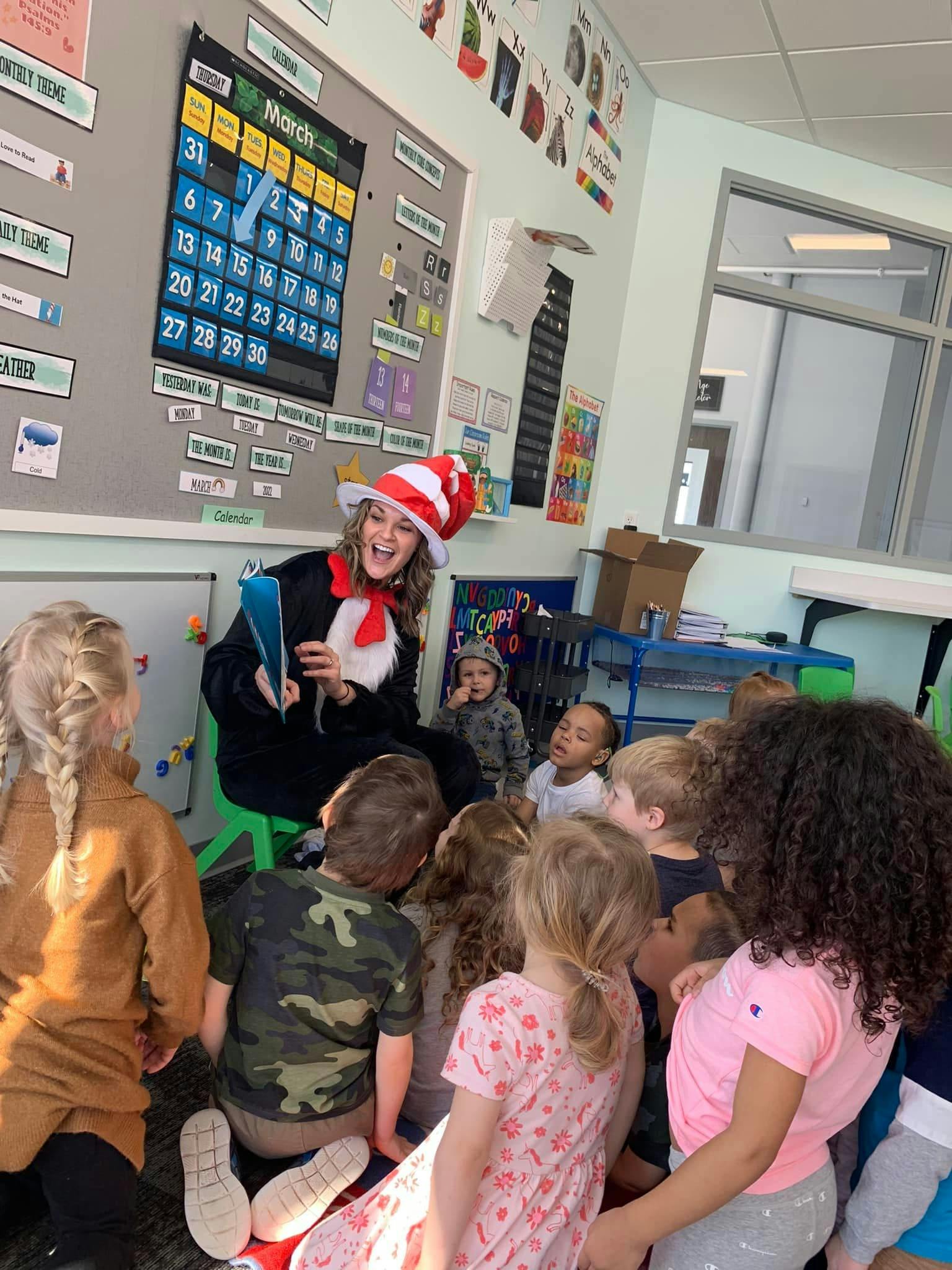 Person in a red and white striped hat reading to children in a classroom