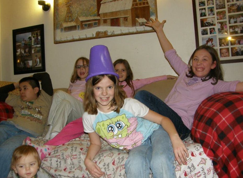 Child with a purple bucket on their head sitting on a couch with other children