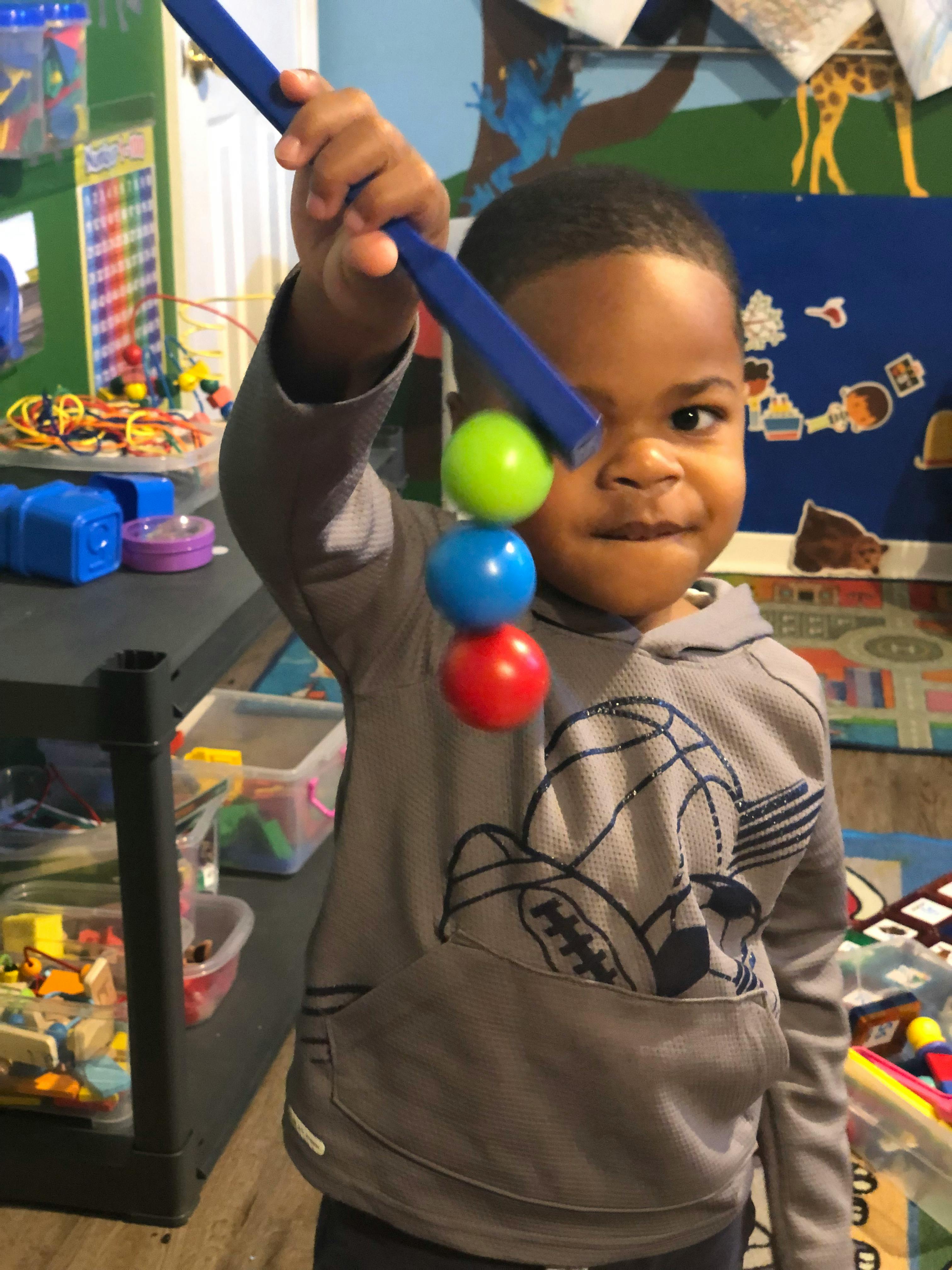 Child holding a blue stick with three colorful balls attached