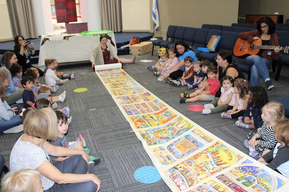 Adults and children sitting on floor around long illustrated scroll
