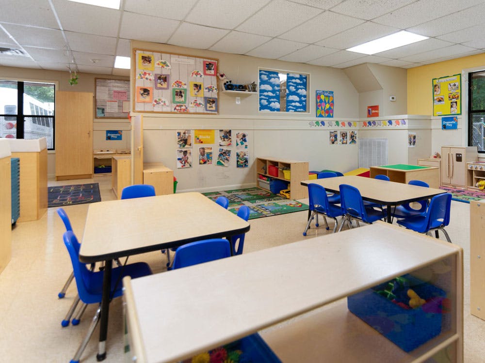 An empty daycare classroom with tables, blue chairs, and children's furniture