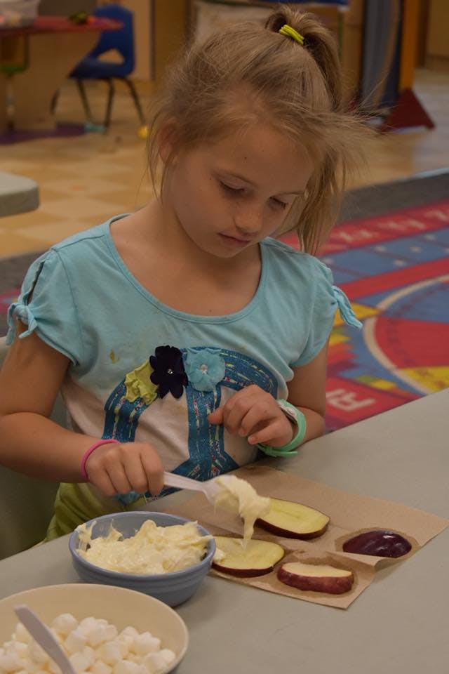 Child spreading a white substance on apple slices