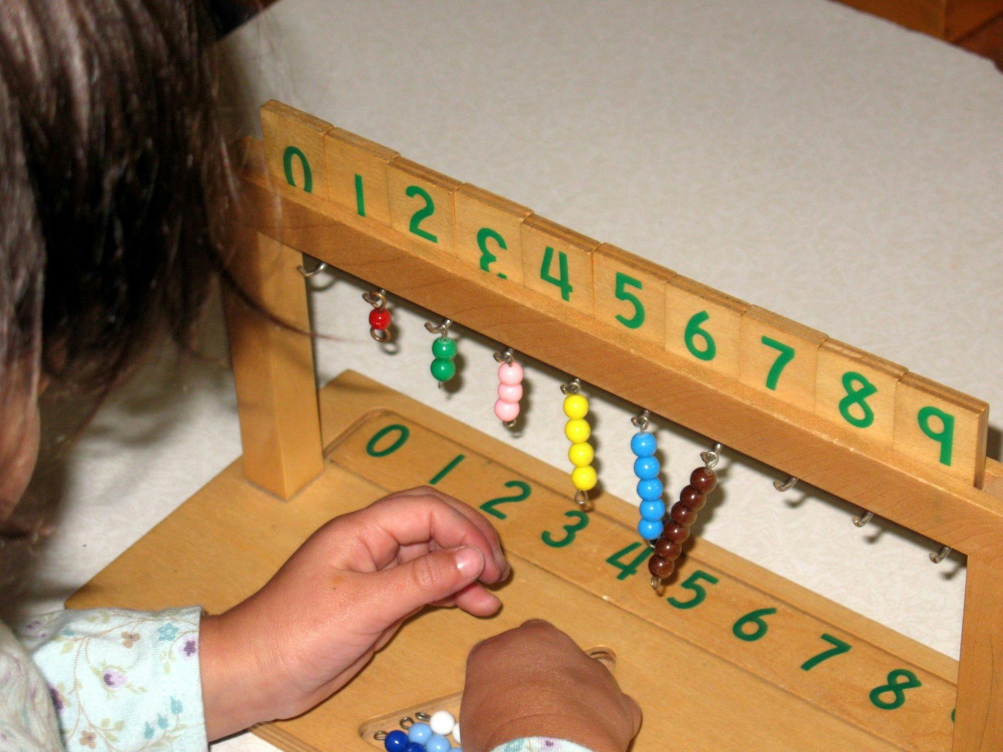 Child's hands interacting with a wooden counting frame with beads and numbers
