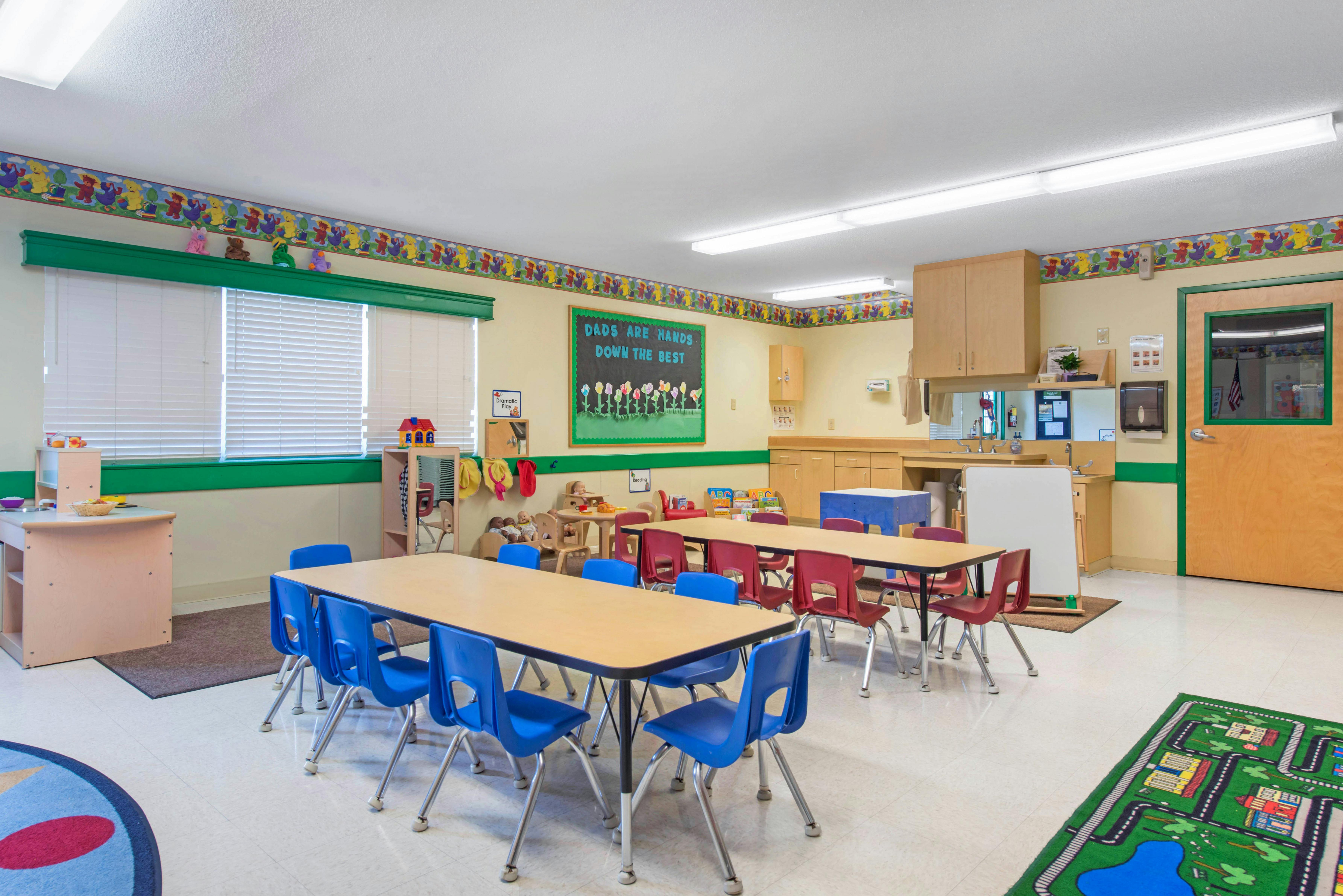 Classroom with small tables and chairs, play kitchen, and wall decor