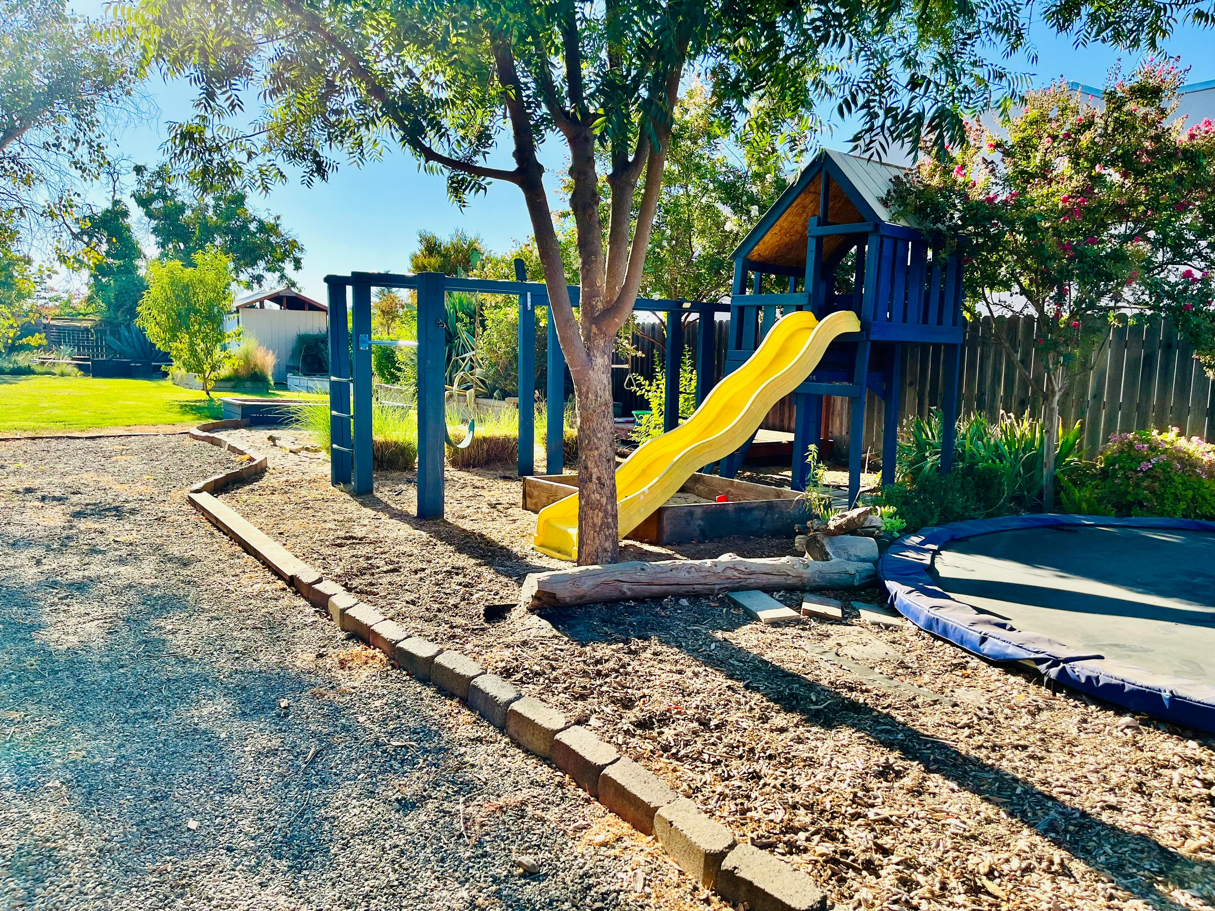 Playground with blue playset, yellow slide, and trampoline