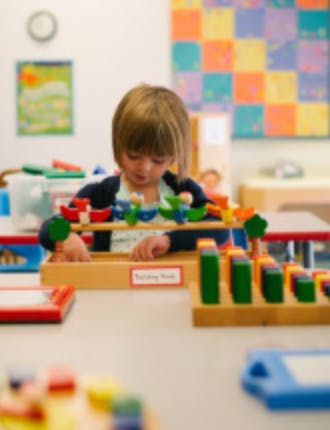 Child playing with colorful wooden blocks and a counting frame in a classroom