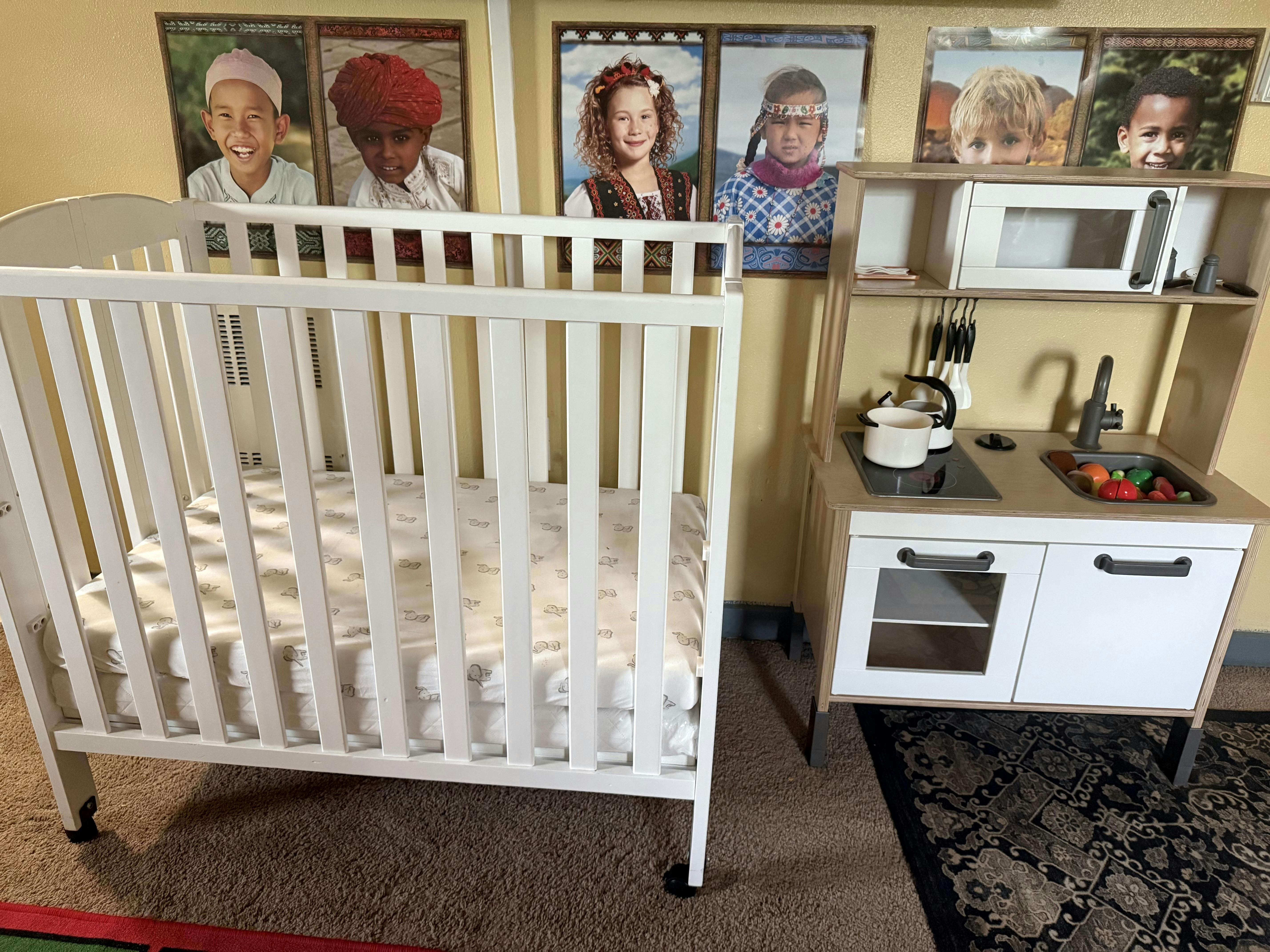 White crib next to a child's play kitchen set